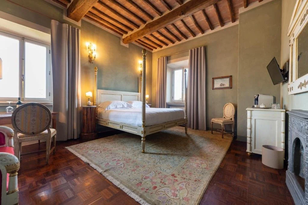 Foto eines klassischen Schlafzimmers mit olivgrünen Wänden, rustikaler Holzbalkendecke und einem hellen Himmelbett, das auf einem großen Teppich über dunklem Holzparkett steht.