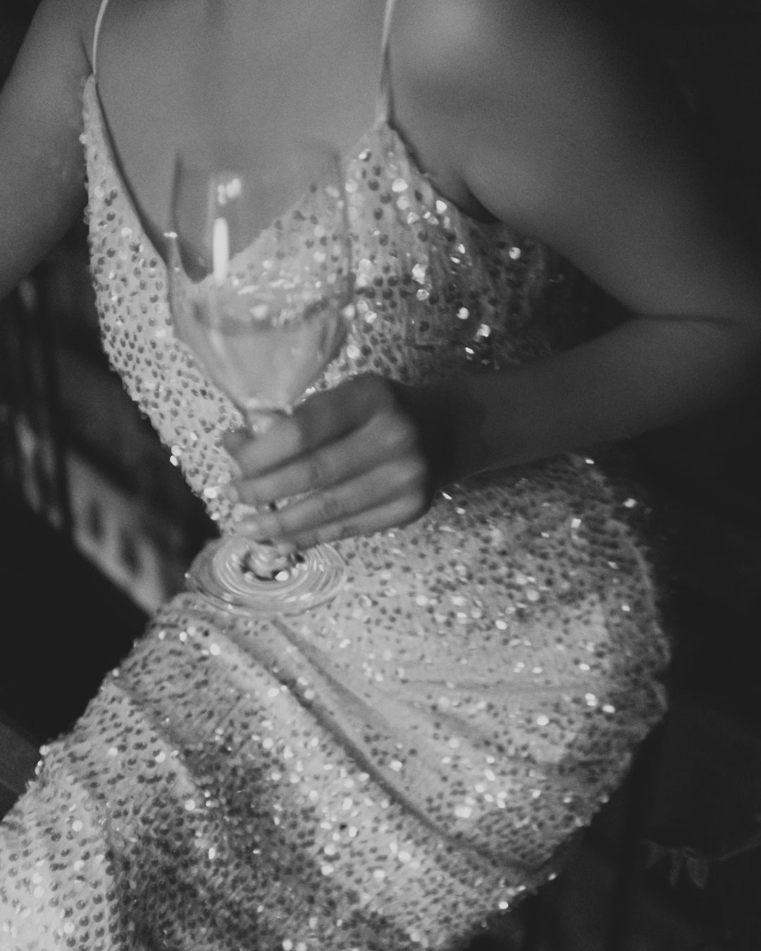 Nahaufnahme einer Person in einem funkelnden, glitzernden Kleid, die ein Gläschen Champagner hält.