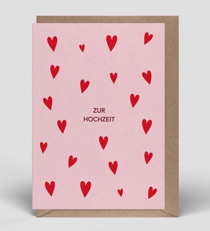 Zartrosa Glückwunschkarte zur Hochzeit mit einem Muster aus vielen kleinen, roten Herzen und dem schlichten, zentrierten Schriftzug „ZUR HOCHZEIT“.