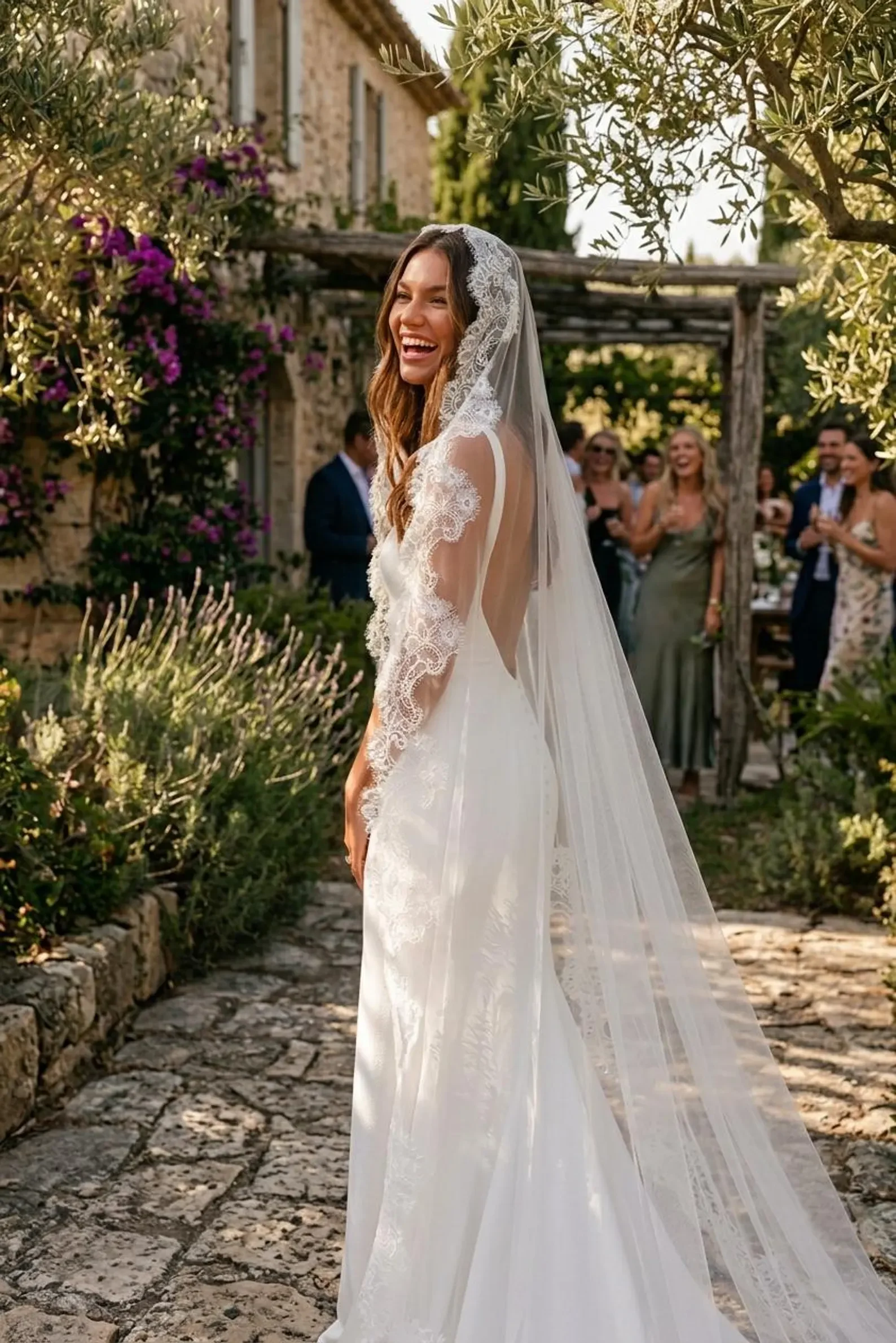 Lachende Braut bei einer Outdoor-Hochzeit im rückenfreien Kleid und langen Mantilla-Schleier mit edler Spitzenkante. Inspiration für den Brautschleier-Guide.