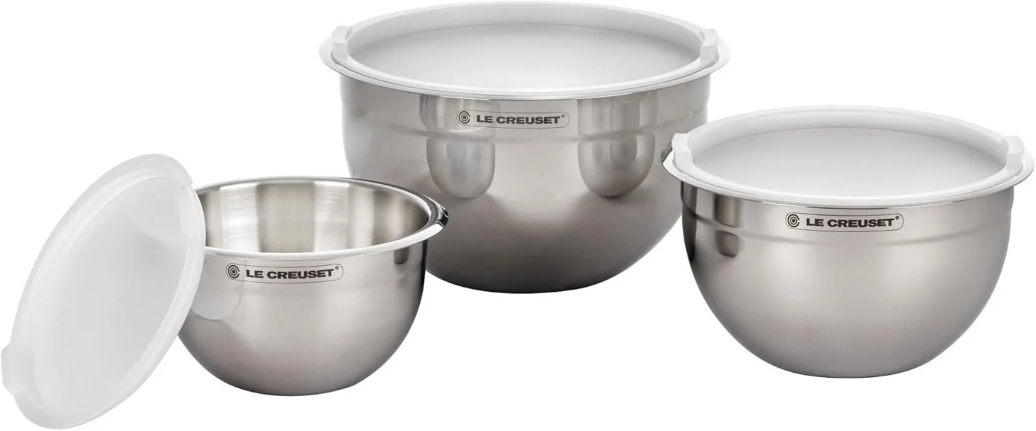 Drei unterschiedlich große Edelstahl-Rührschüsseln von Le Creuset mit weißen Deckeln. Zwei sind verschlossen, bei der kleinsten lehnt der Deckel offen daneben.