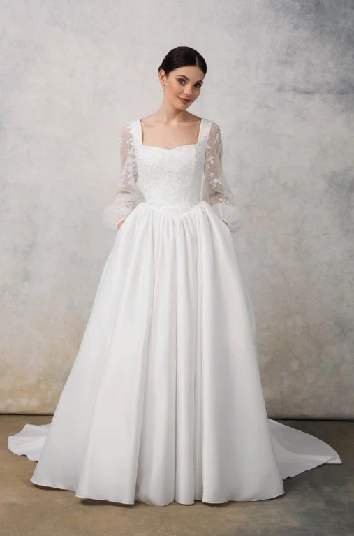 Klassisches Brautkleid mit eckigem Ausschnitt, langen Ärmeln aus bestickter Spitze und einem voluminösen, glatten Rock mit praktischen Taschen.