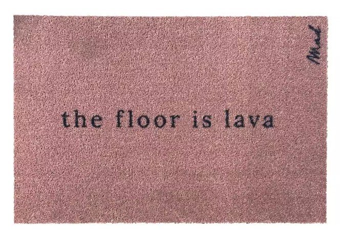 Einfarbige Fußmatte in Altrosa mit dem schwarzen, humorvollen Schriftzug „the floor is lava“ in Schreibmaschinen-Optik.