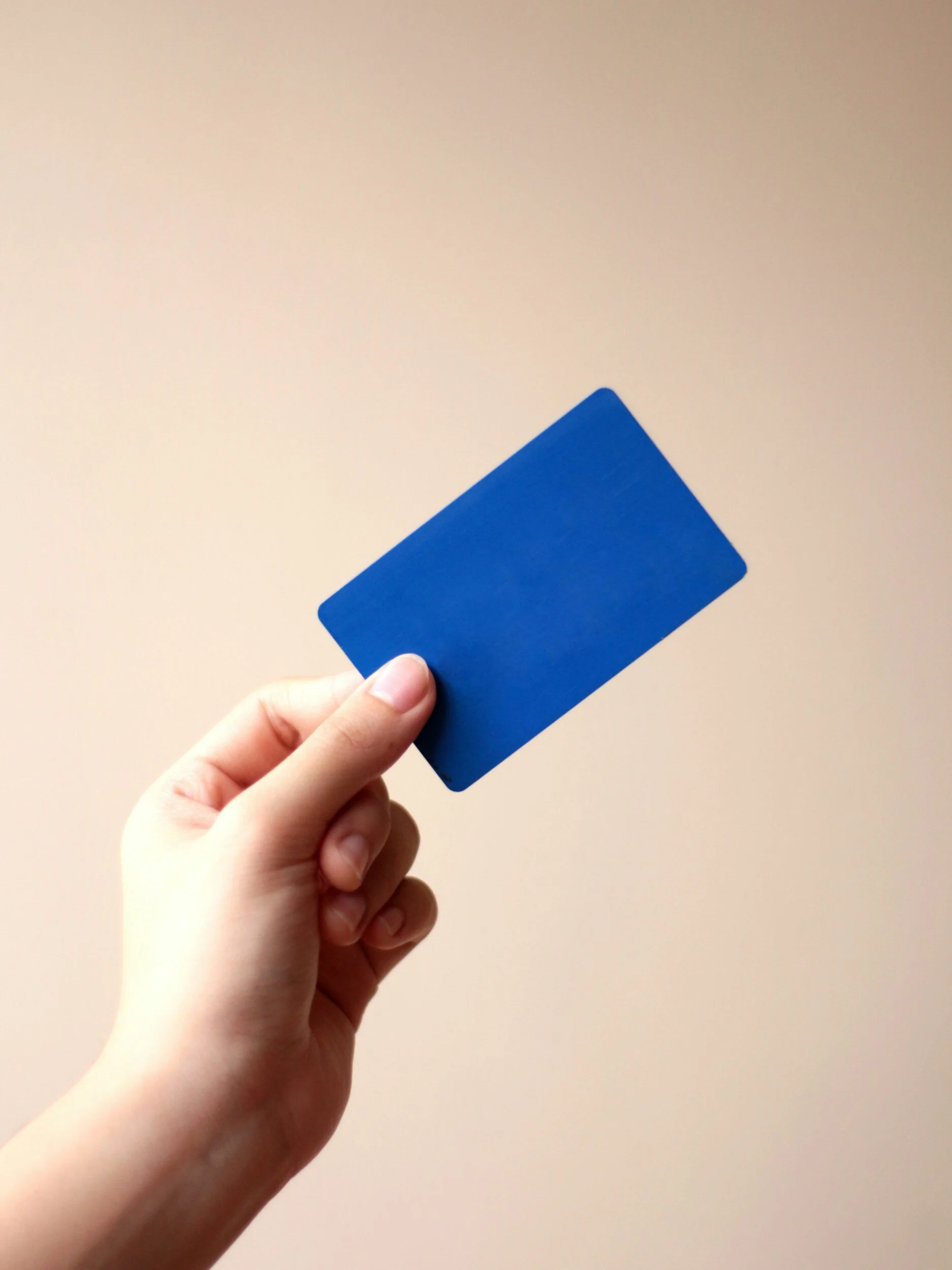 Hand holding a blue card against a beige background.