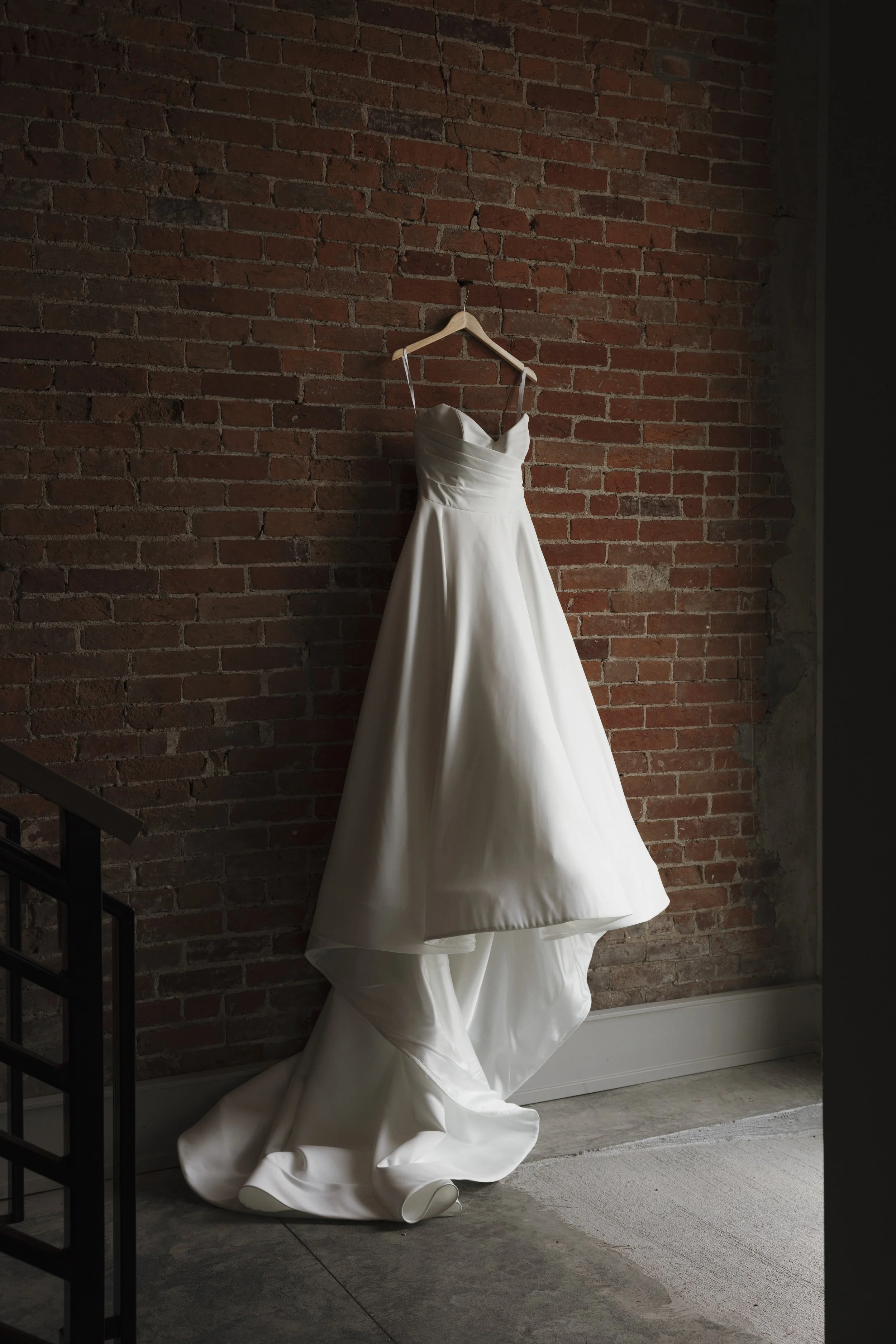 White wedding dress hanging on a hanger against a red brick wall.