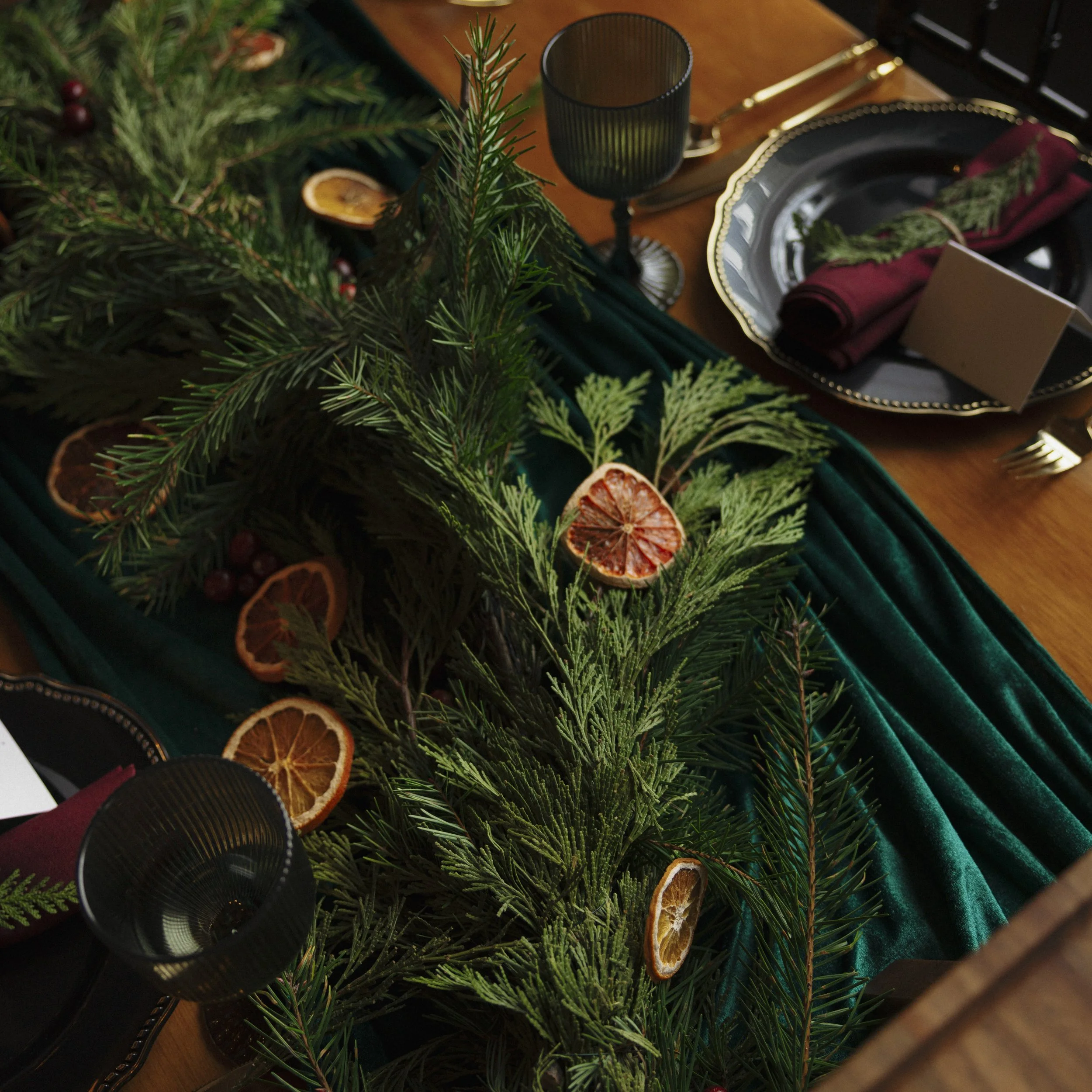 A holiday table centerpiece with evergreen branches and dried orange slices.