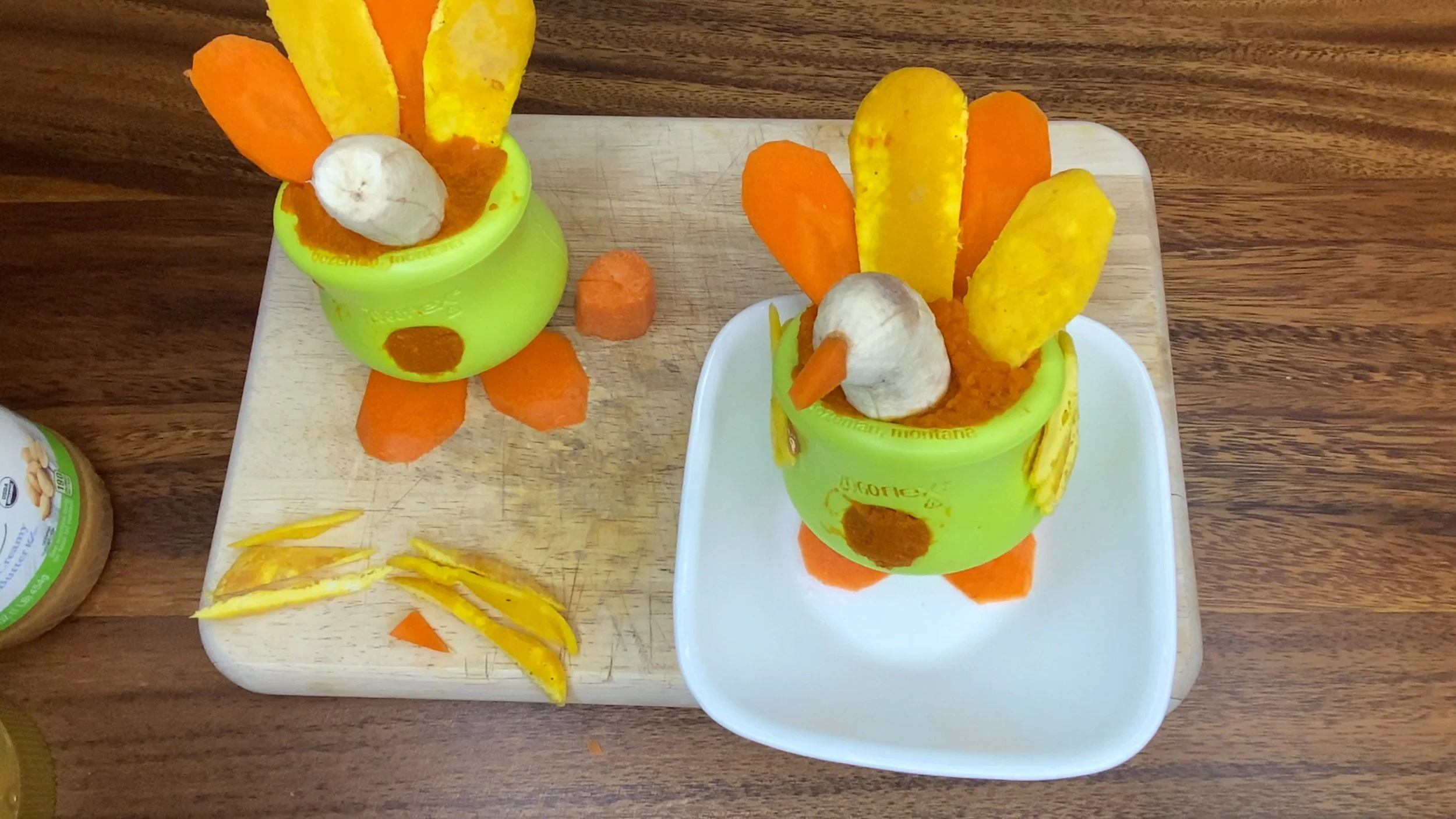Two stuffed, green West Paw Zogoflex Toppls (one in a dish) sitting on top of a cutting board