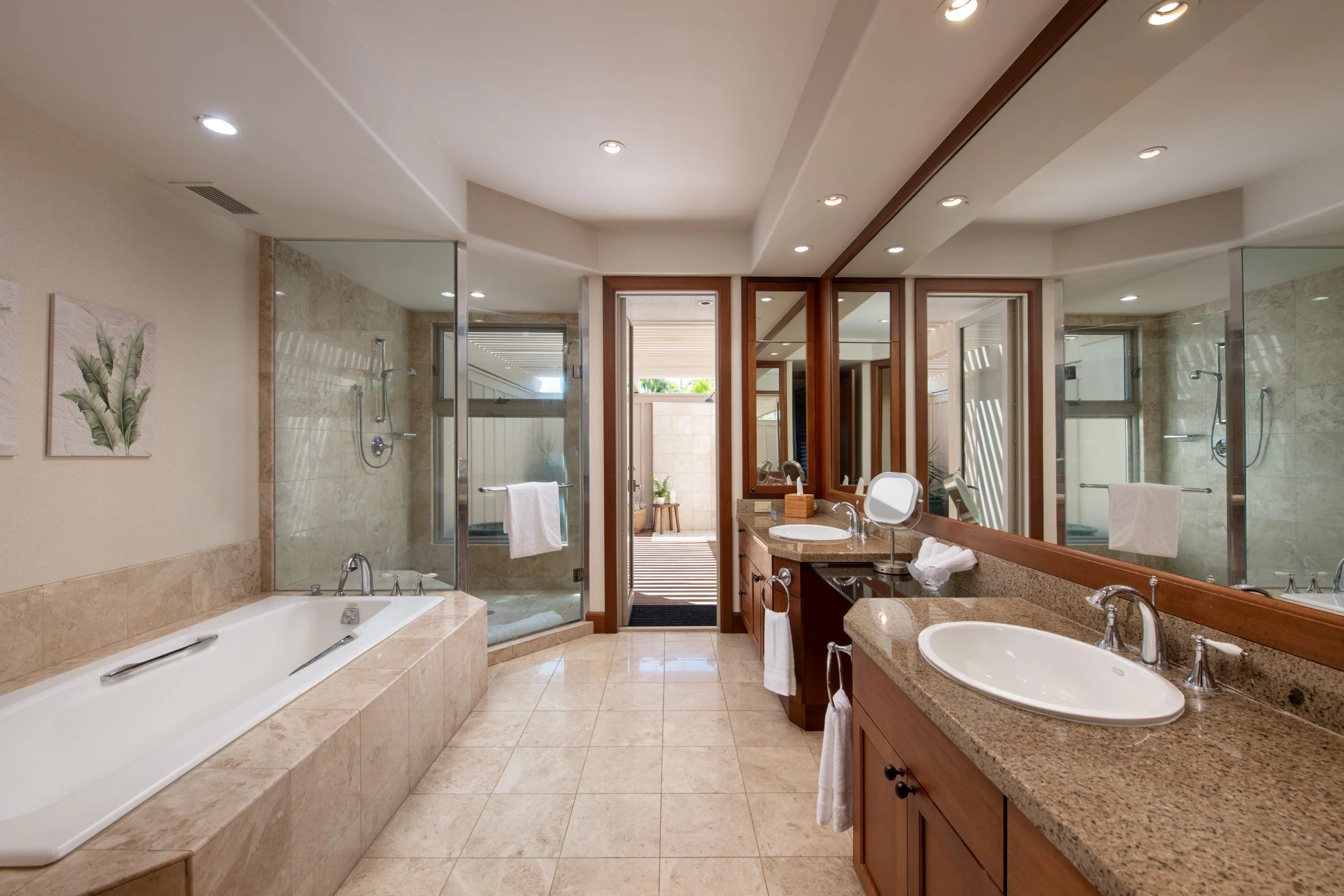 The primary bathroom includes dual marble-topped vanities, warm mahogany cabinets, a spacious soaking tub, and a walk-in shower.