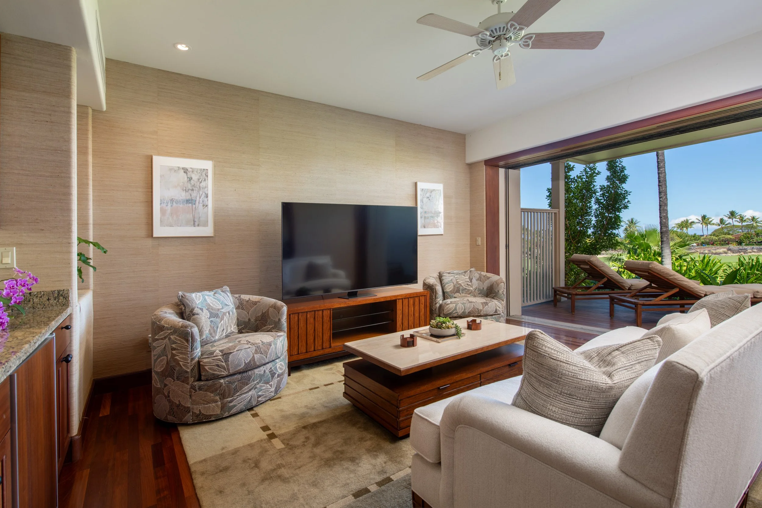 Lower-level media room with pocket doors opening to the lanai showcases the 4th fairway of the Hualalai Golf Course and the Pacific Ocean.