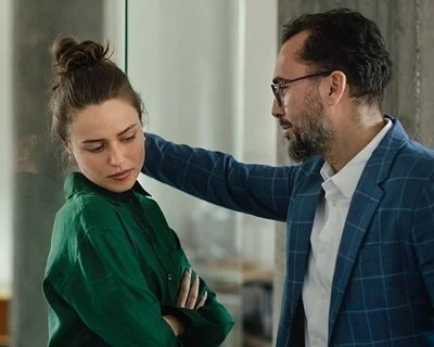 A man with his arm on a wall, uncomfortably close to a woman who is looking away