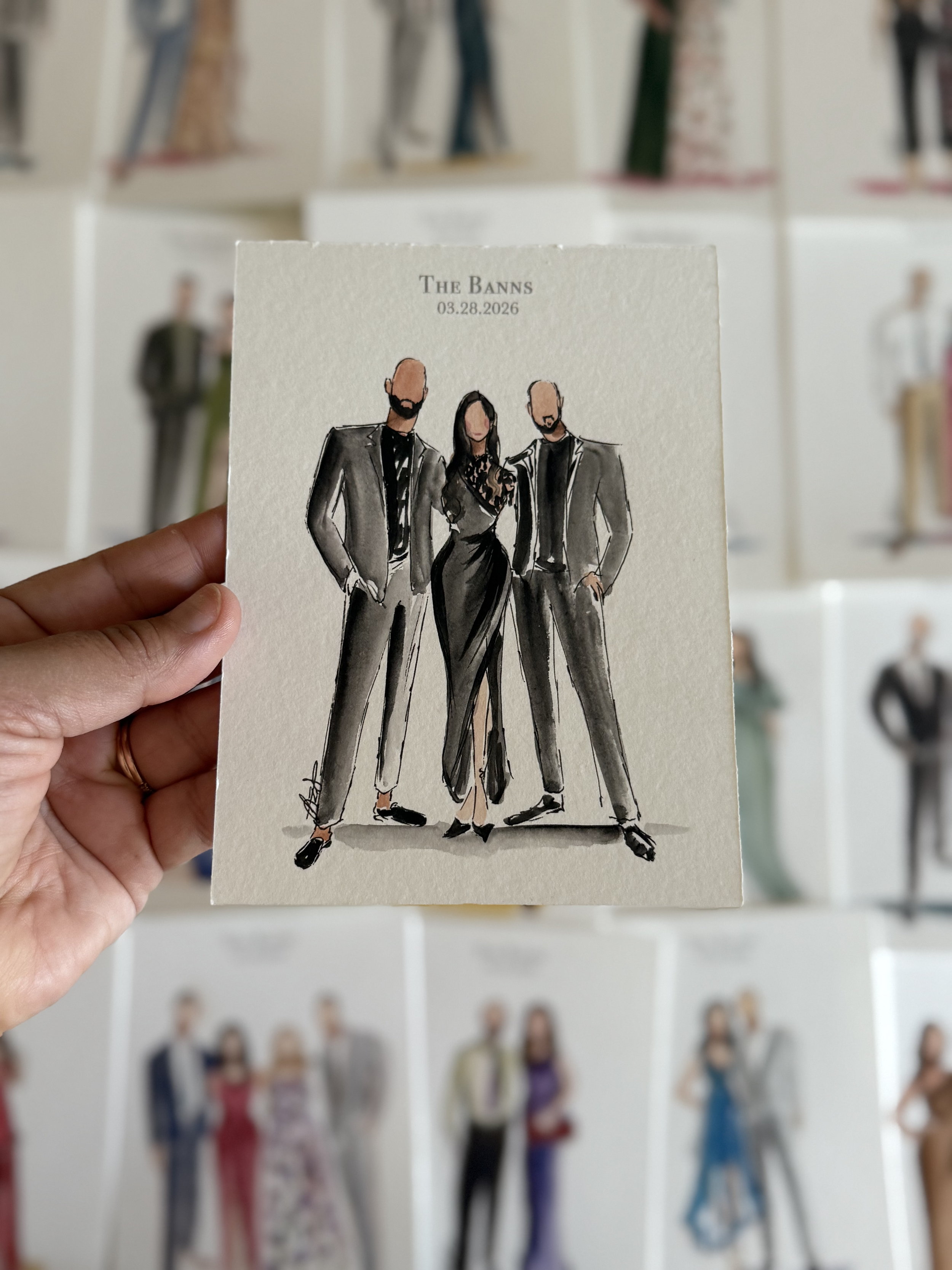 Hand holding a illustrated card of three fashionable people, with a blurred background of other similar cards.