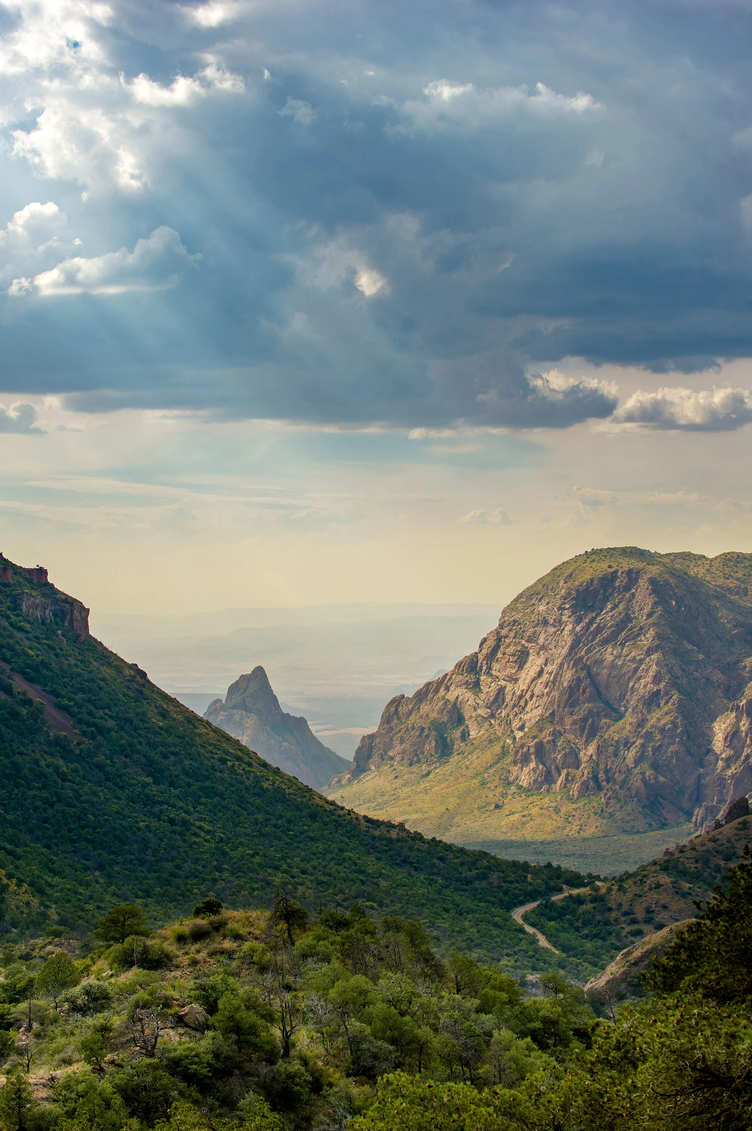 Scenic view of green mountains with a winding road and a cloudy sky overhead.