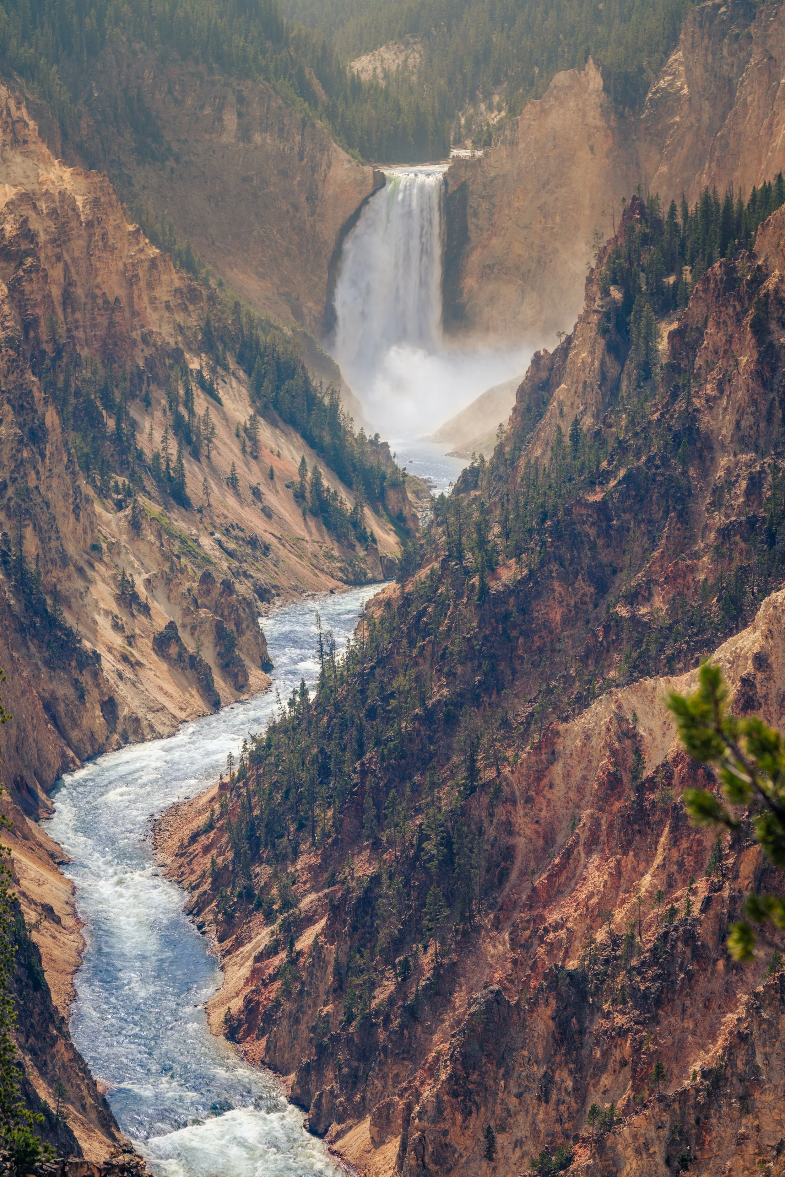 A waterfall cascading down a canyon with a river flowing through the rocky landscape, surrounded by pine trees and rugged cliffs.