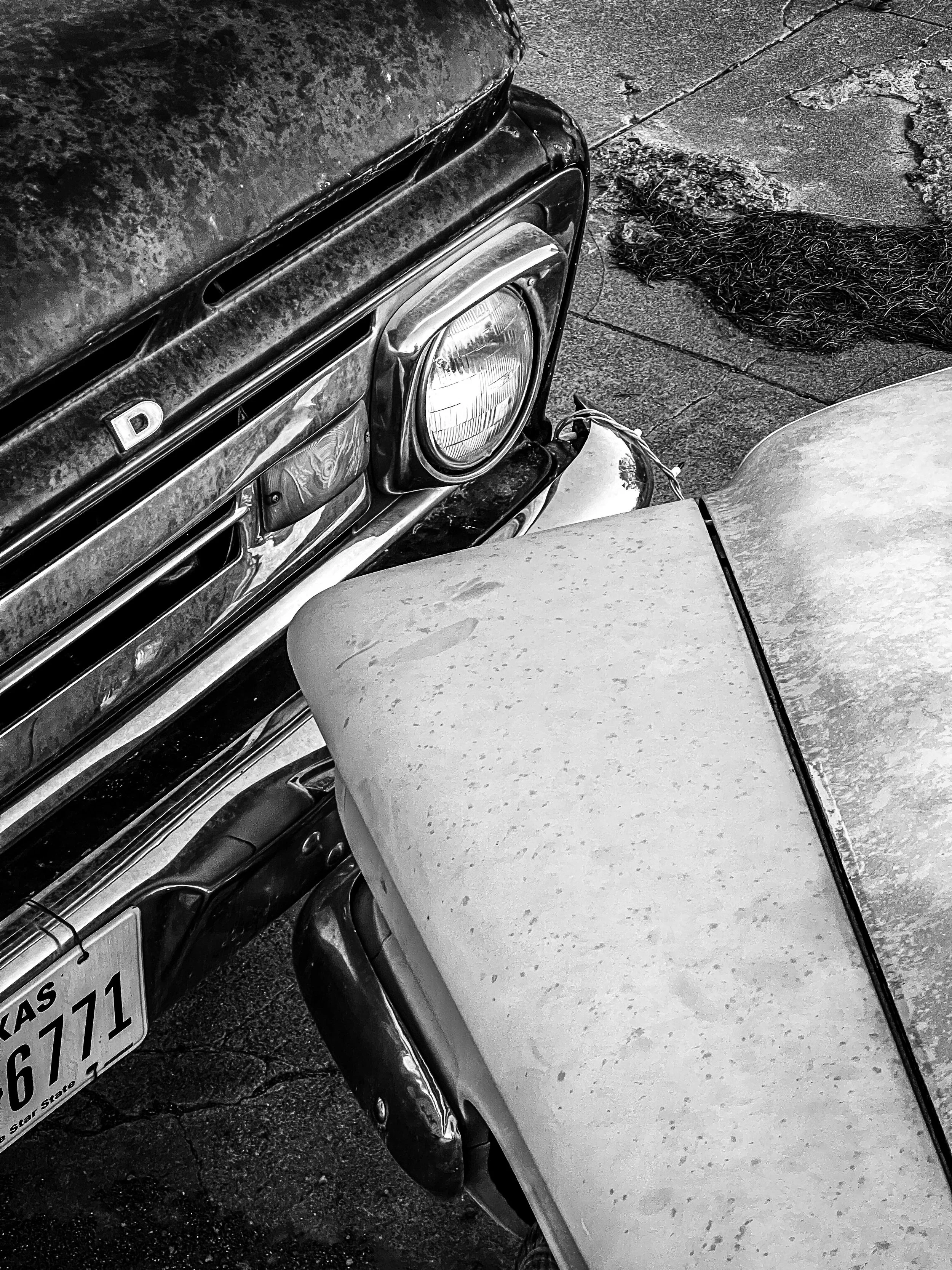 Close-up of the front grill and hood of an old, weathered black classic car with a Texas license plate, parked on a rough asphalt surface.