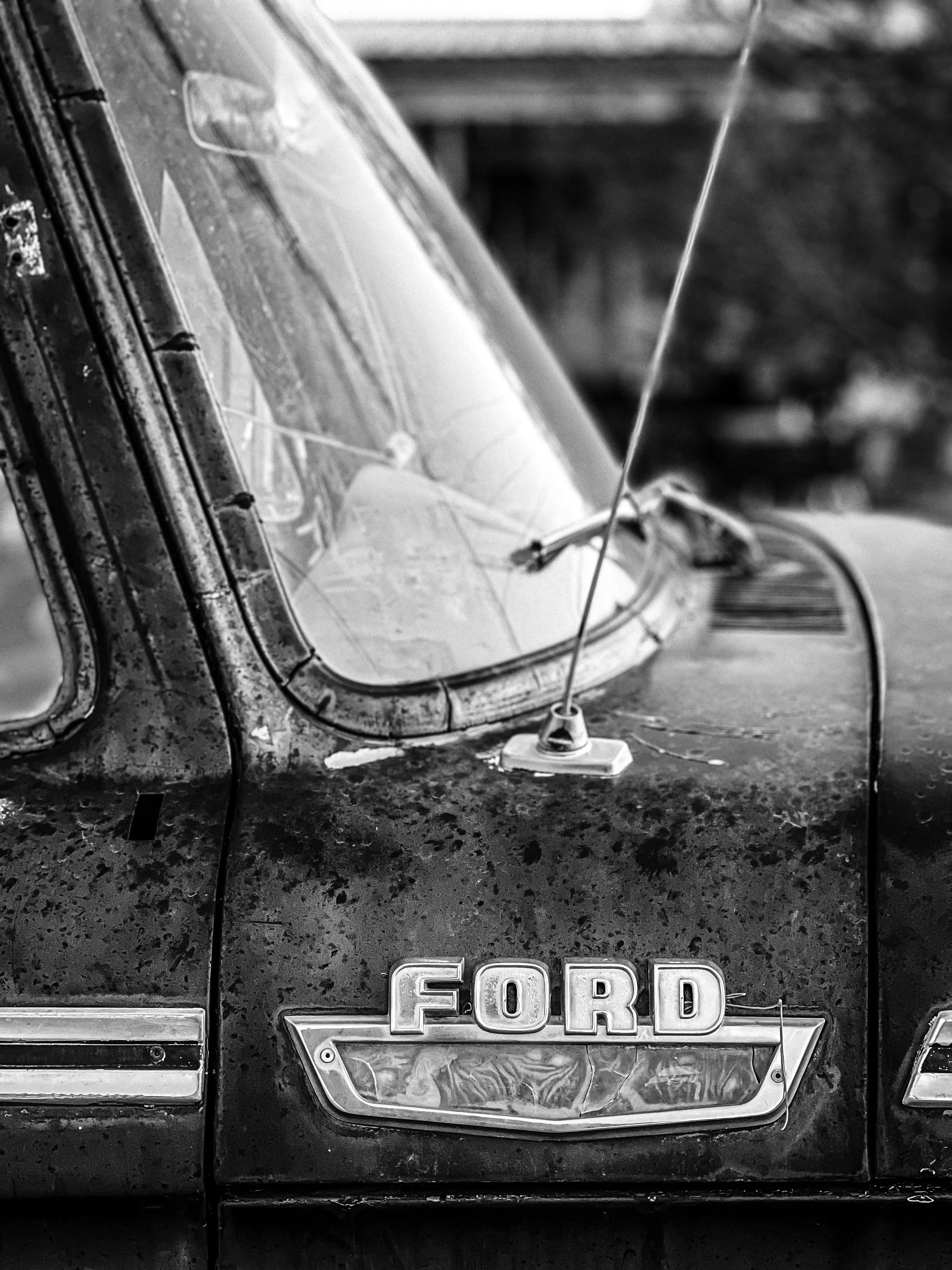 Close-up of an old, rusty Ford car with a dirty windshield and an antenna.