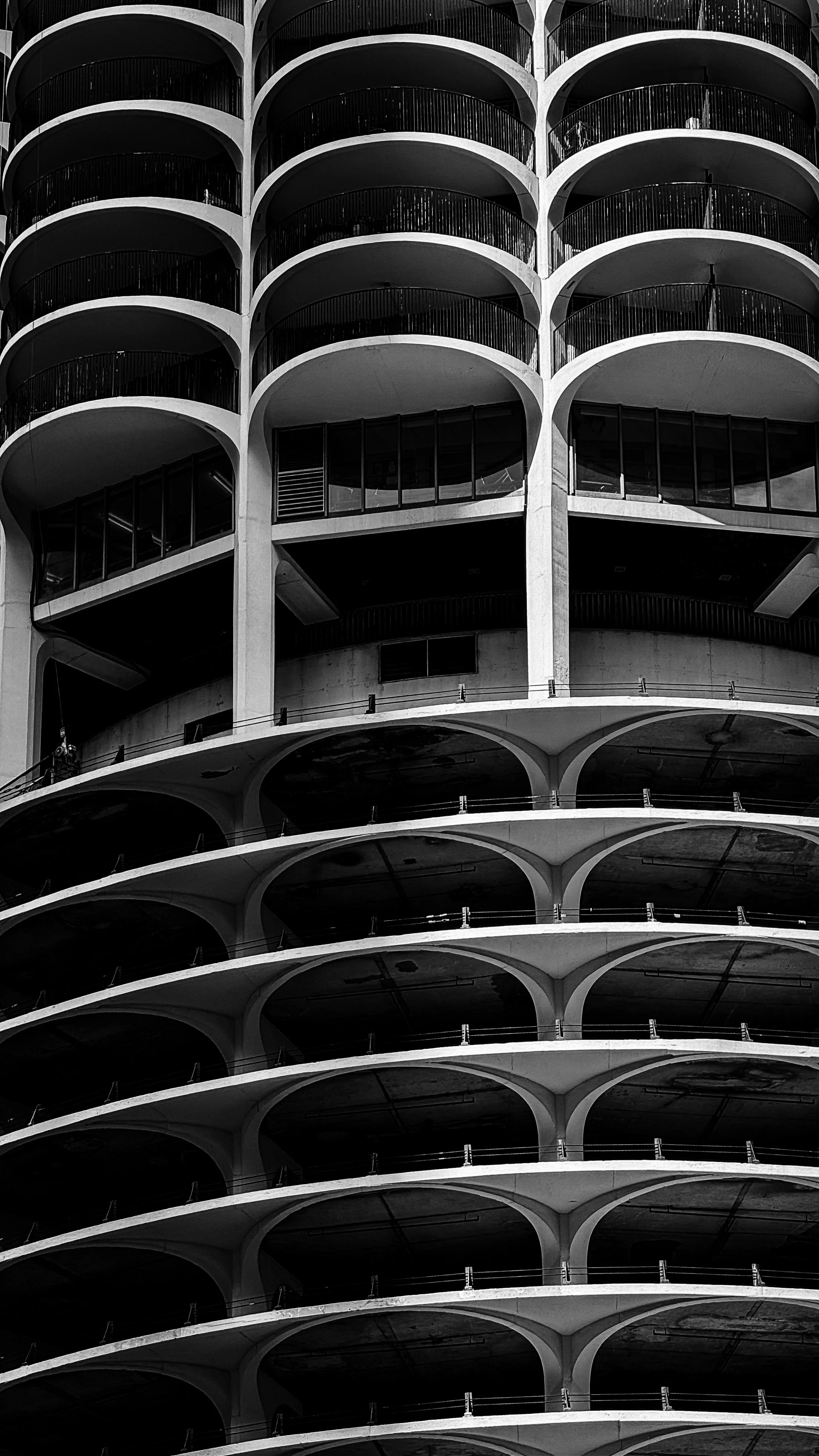 Black-and-white photo of a multi-story building with rounded balconies on each floor, creating a repeating pattern of arches.