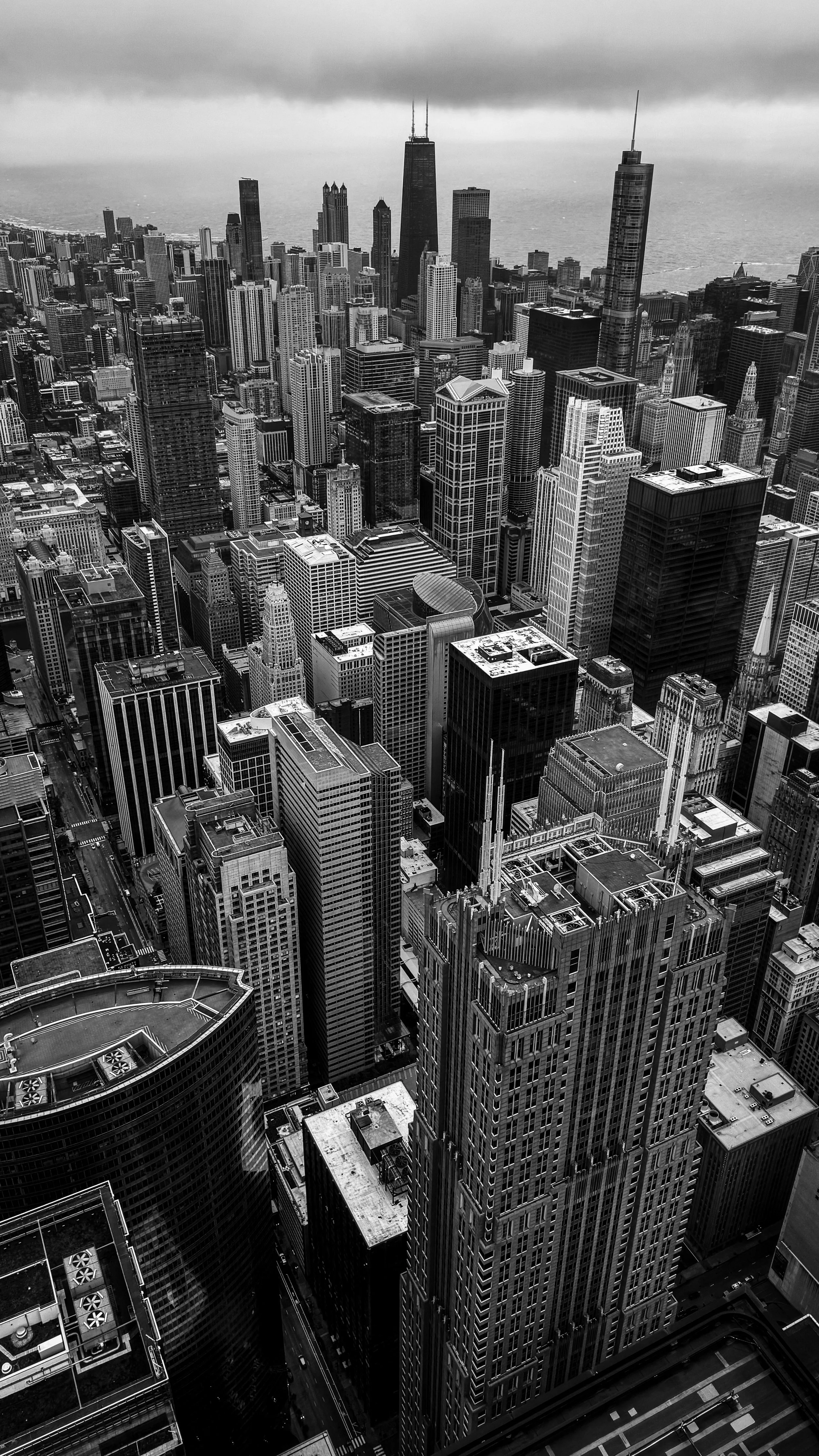 Black and white aerial view of Chicago skyline with numerous skyscrapers and Lake Michigan in the background.