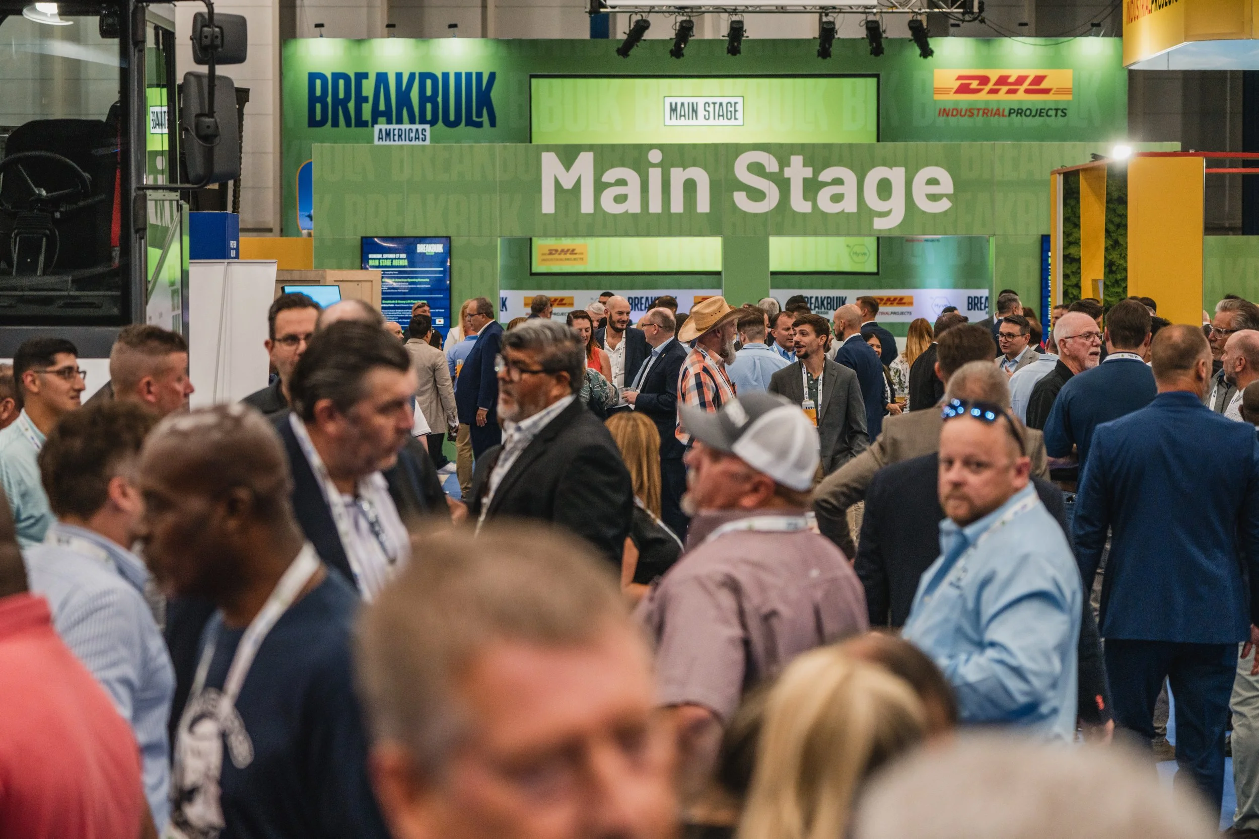 Crowd of people attending a conference or trade show in front of a large green sign that reads 'Main Stage' with the logos of Breakbulk and DHL, inside a convention center.