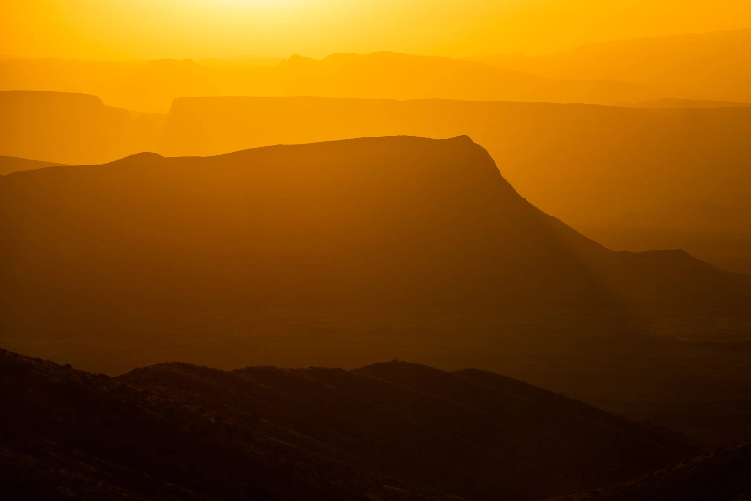 Silhouettes of layered mountains during sunset with an orange sky.
