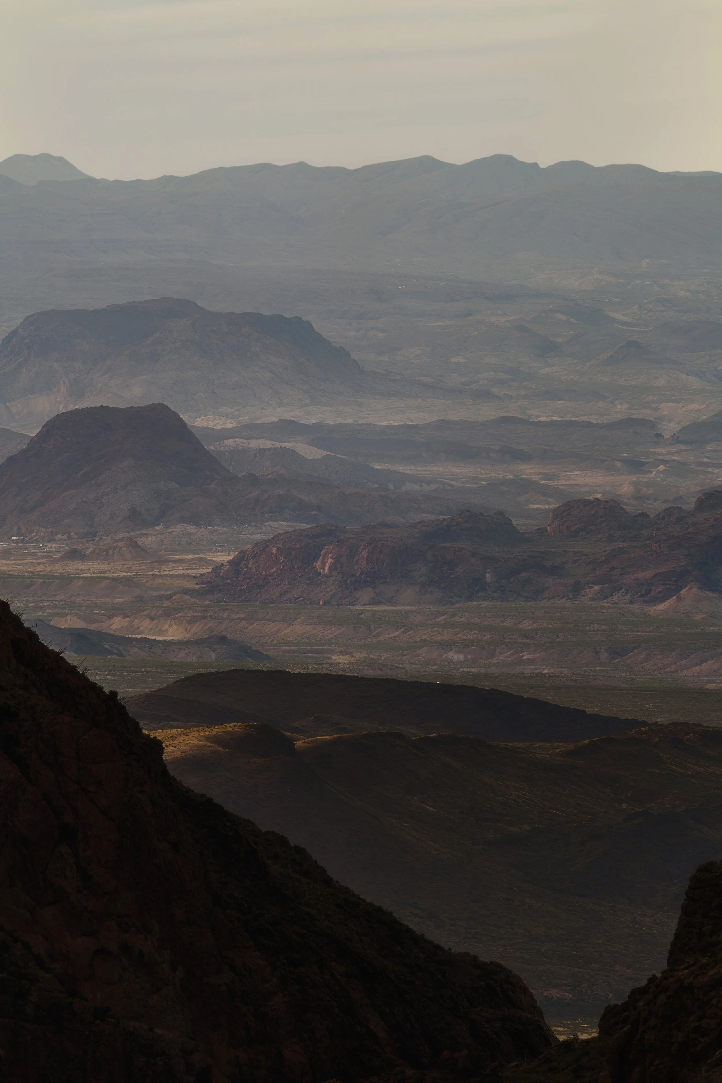 A scenic view of layered mountains and valleys with varying shades of earthy colors and rugged terrain.