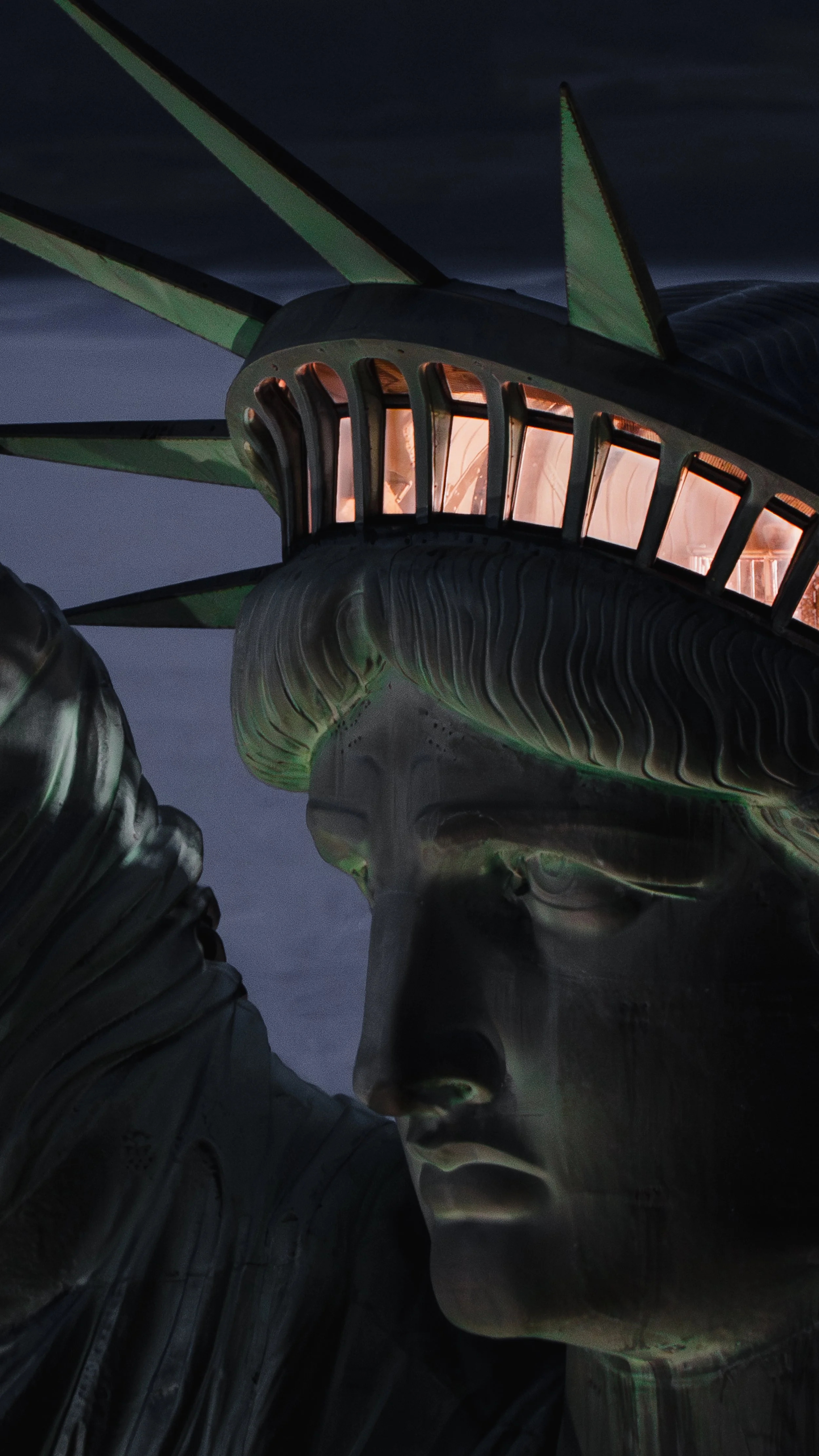 Close-up of the Statue of Liberty's face and crown at night, with a dark sky in the background.