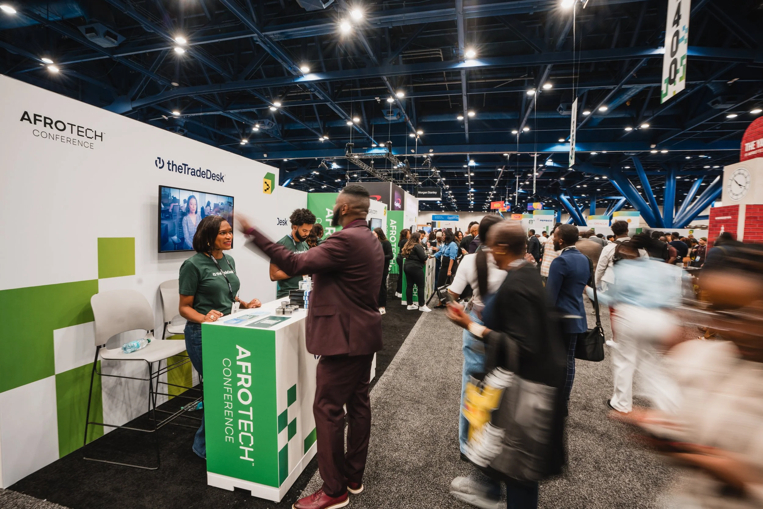 A crowded convention center with a booth for AFROTECH Conference, featuring people engaging at the booth and walking around the exhibit area.