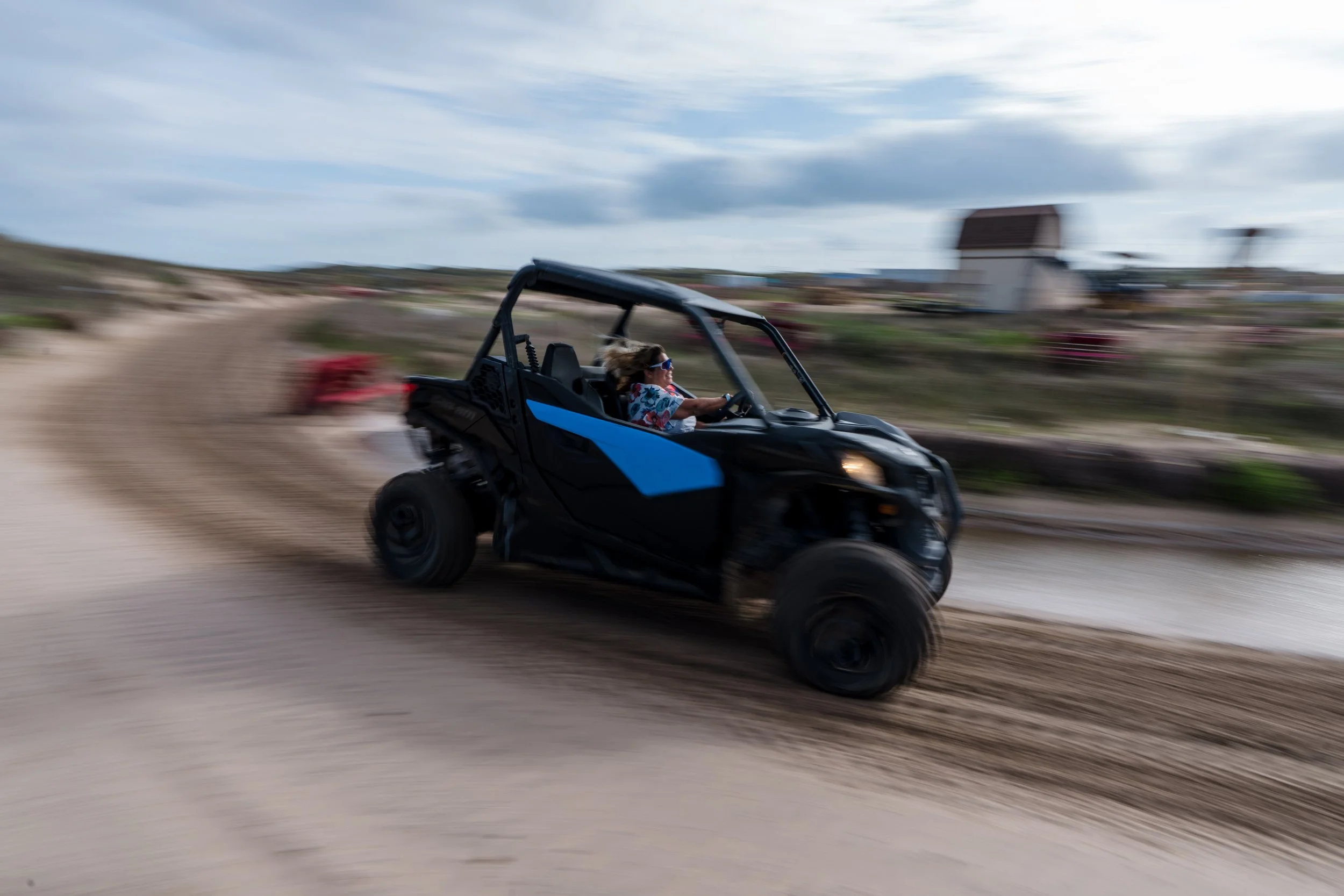 Person driving an off-road utility vehicle on a dirt path, with motion blur indicating high speed against a cloudy sky.