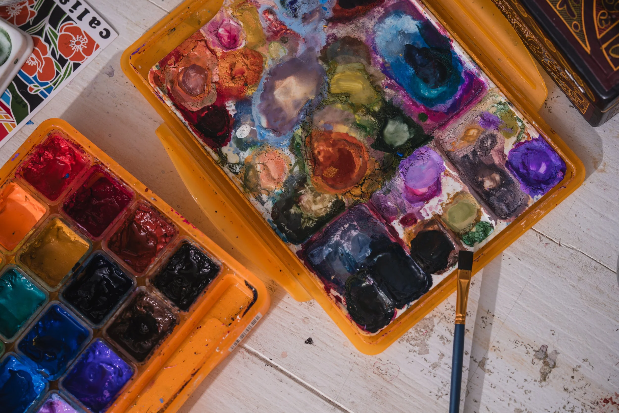 A paint palette and watercolor set with various colors on a white wooden surface.