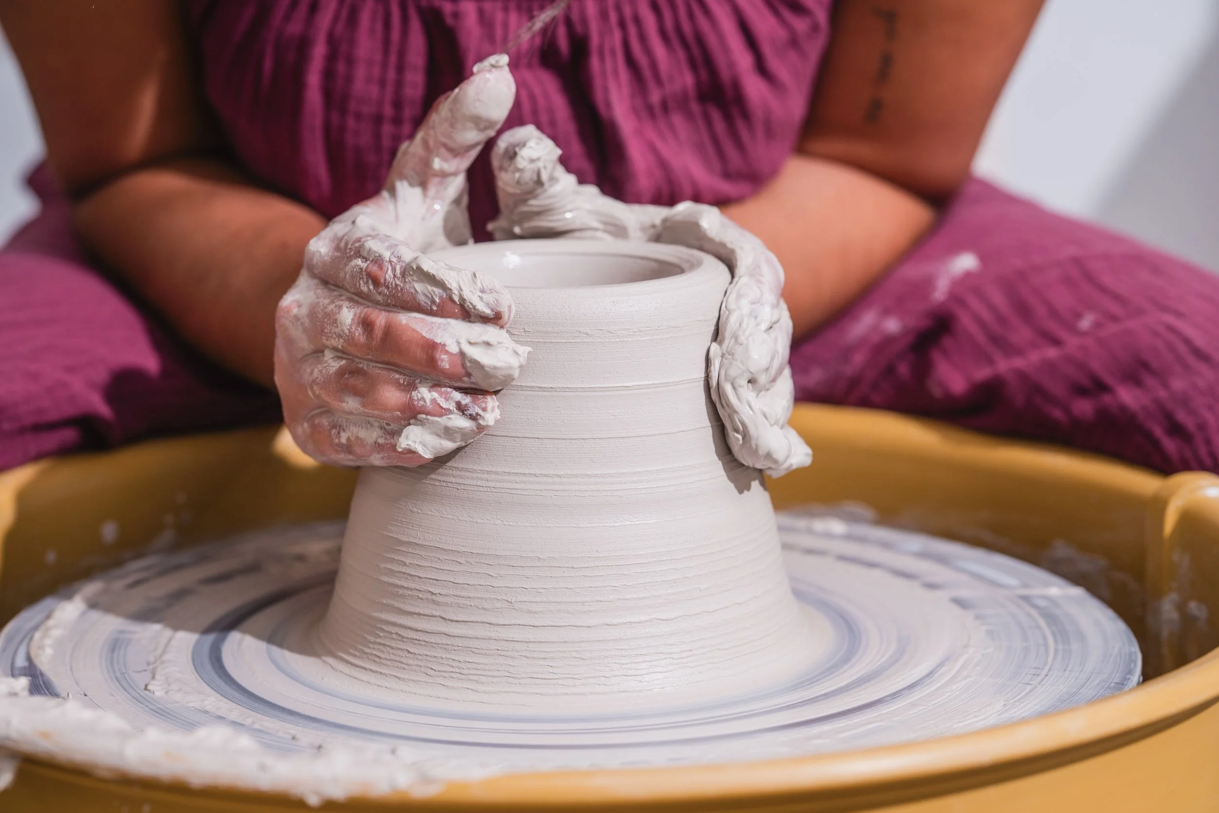 A person shaping a ceramic pot on a pottery wheel, hands covered in wet clay.