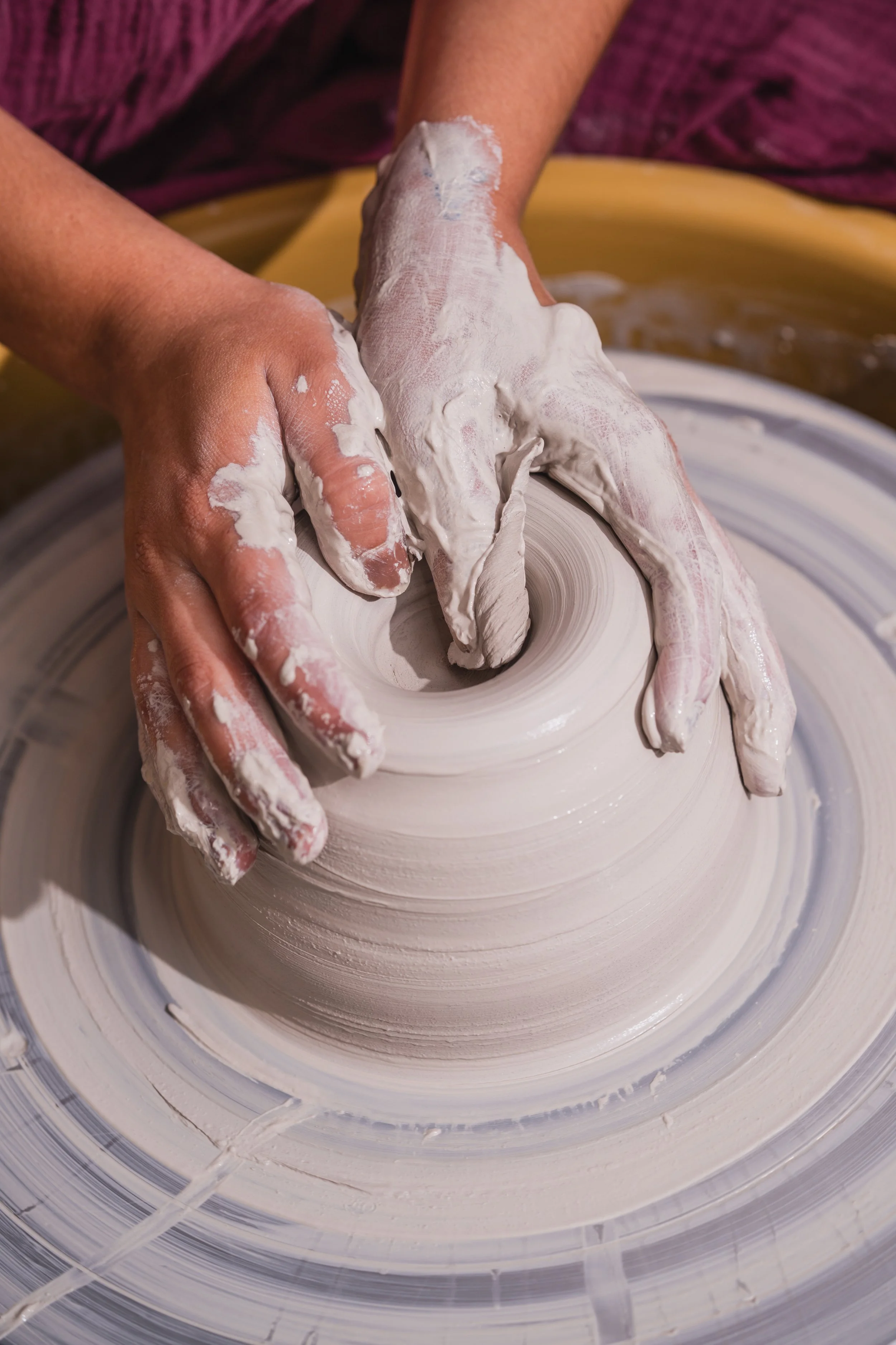Hands shaping wet clay on a pottery wheel to create a ceramic vessel.