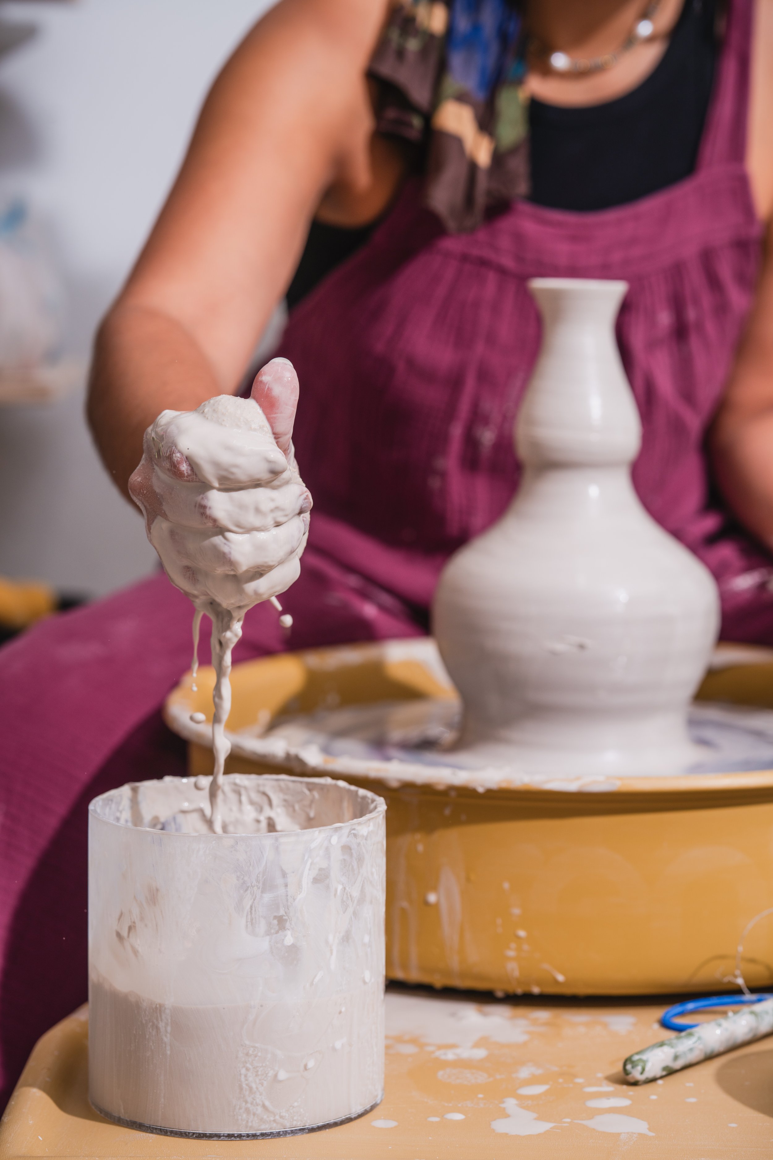 Person sculpting with clay on a pottery wheel with a white vase in progress