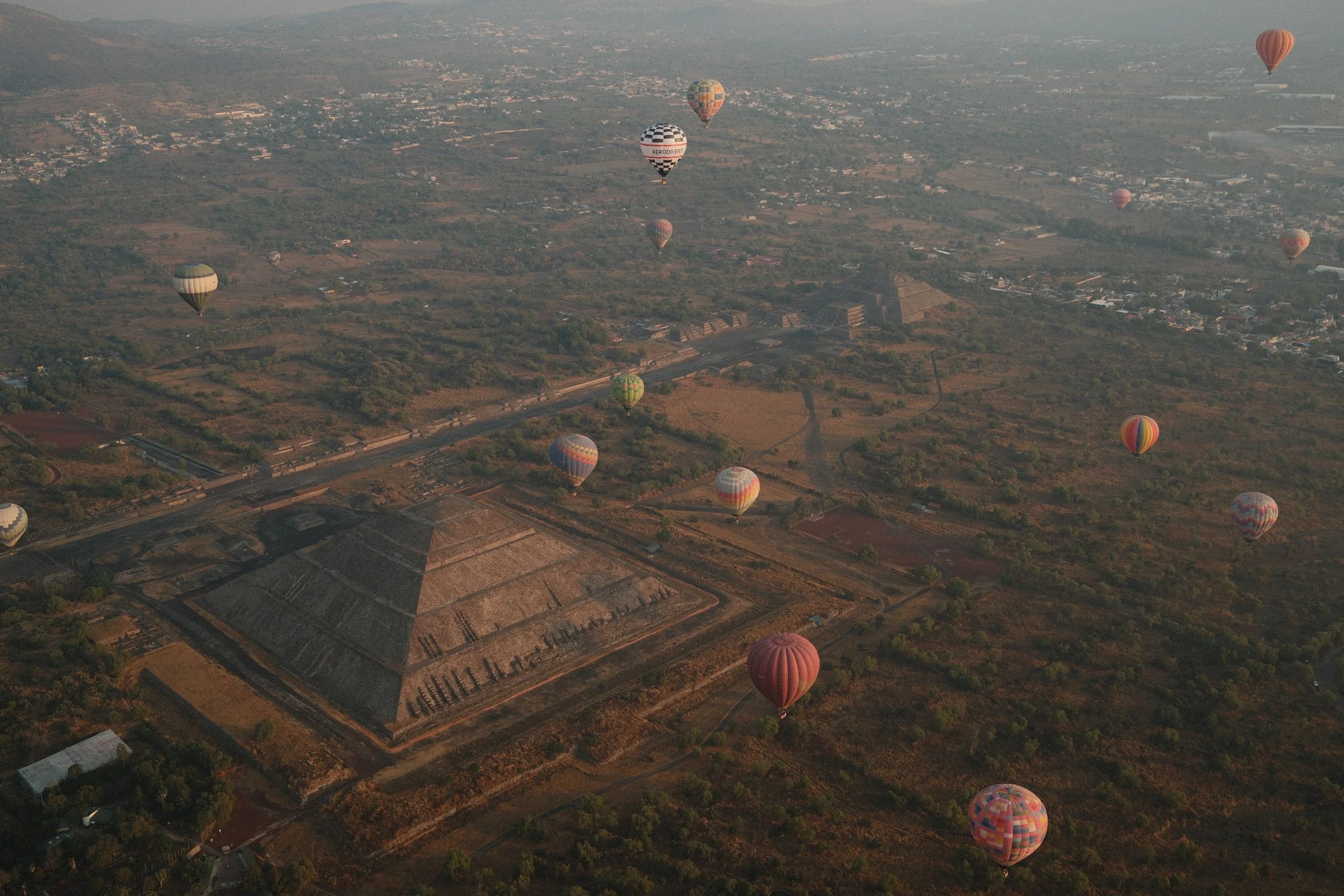 Multiple hot air balloons floating over the ancient Mayan pyramid of Chichen Itza in Mexico during daytime.