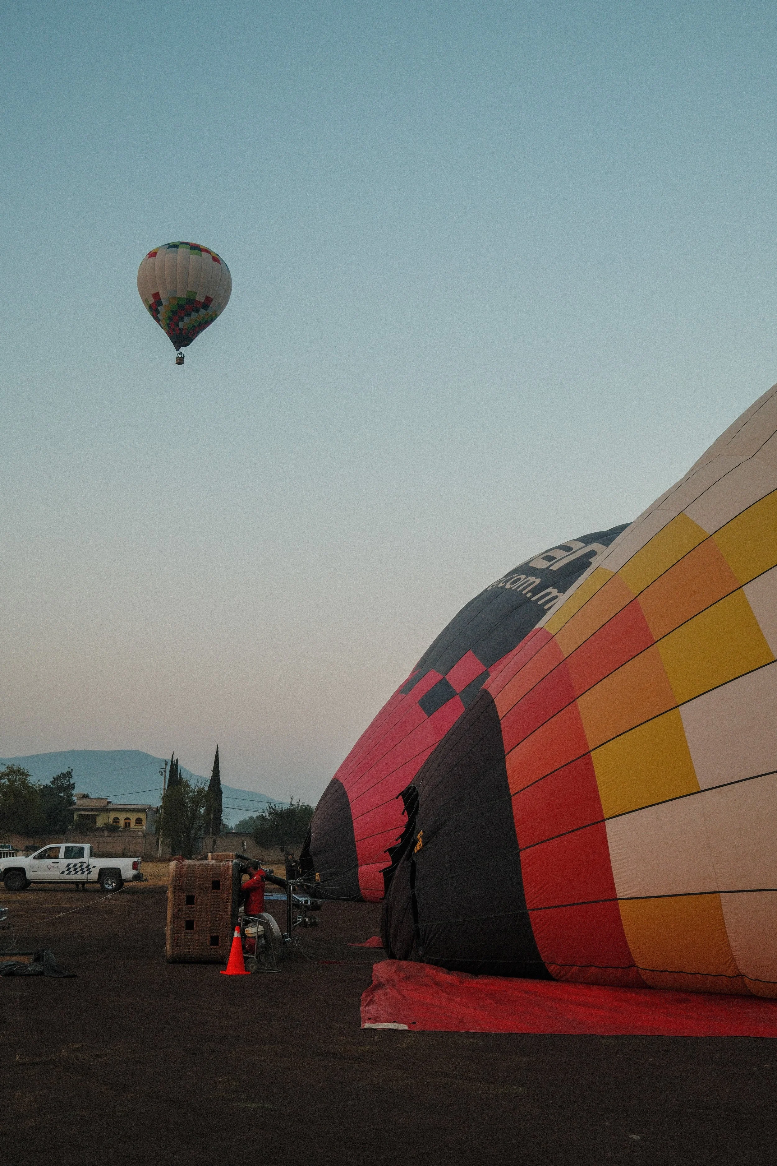 A hot air balloon being prepared for flight on the ground with another hot air balloon already in the sky.