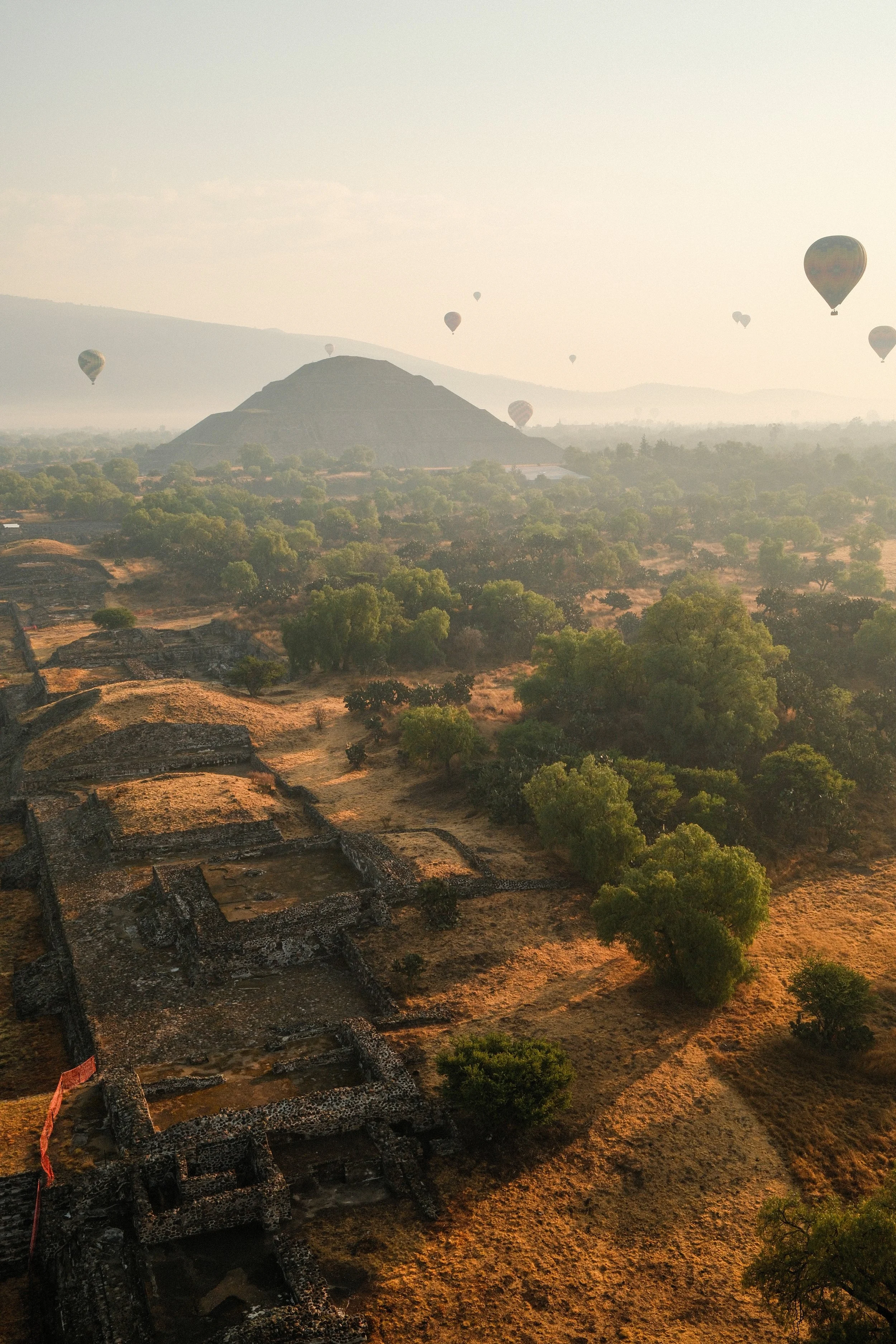 Hot air balloons floating above ancient ruins and a lush landscape at sunrise or sunset.
