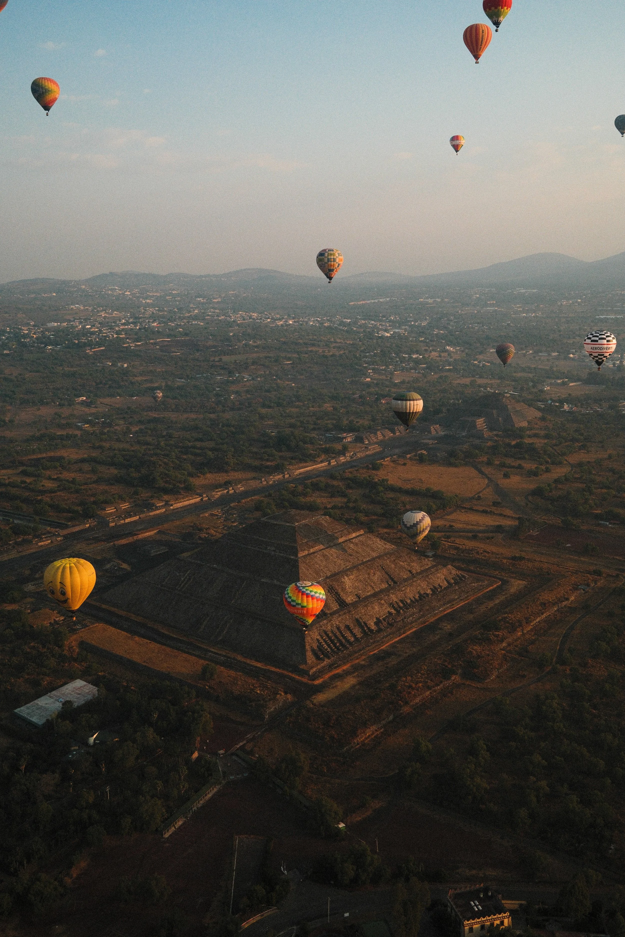 Multiple hot air balloons floating in the sky above the ancient Step Pyramid of Djoser in Saqqara, Egypt, during sunrise or sunset.
