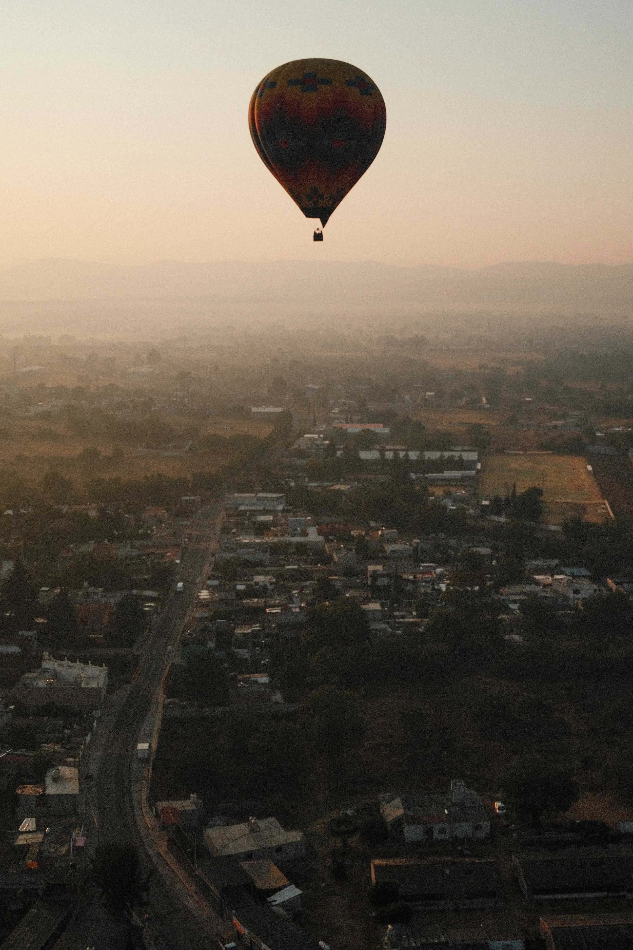Hot air balloon floating above a small town with houses and roads during sunrise or sunset.