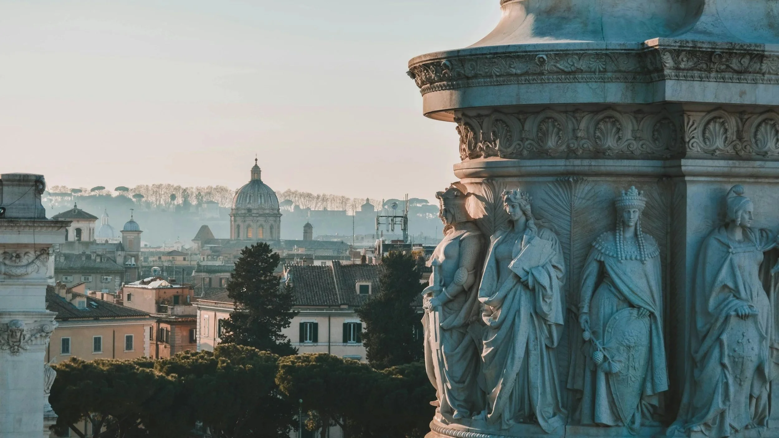 Detailed marble relief sculptures on the Altare della Patria monument overlooking the Rome city skyline and church domes in warm sunlight.