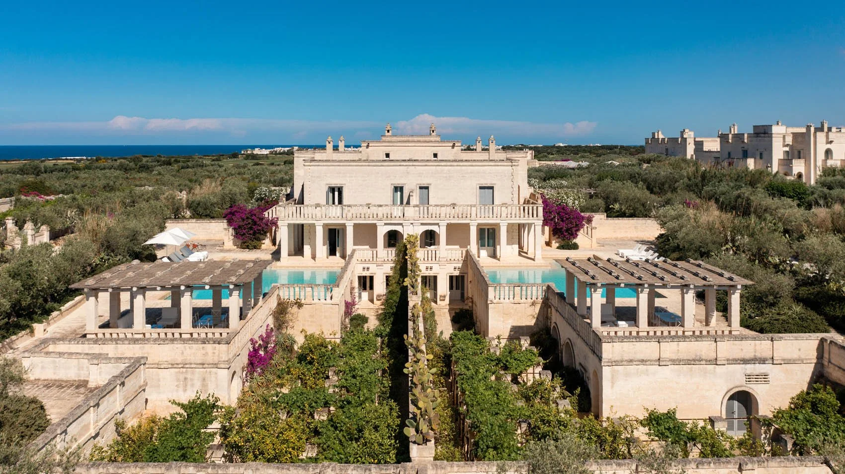 Aerial view of a luxury stone villa at Borgo Egnazia resort featuring private swimming pools, lush courtyards, and vibrant bougainvillea surrounded by olive groves near the Adriatic Sea in Savelletri di Fasano, Puglia.