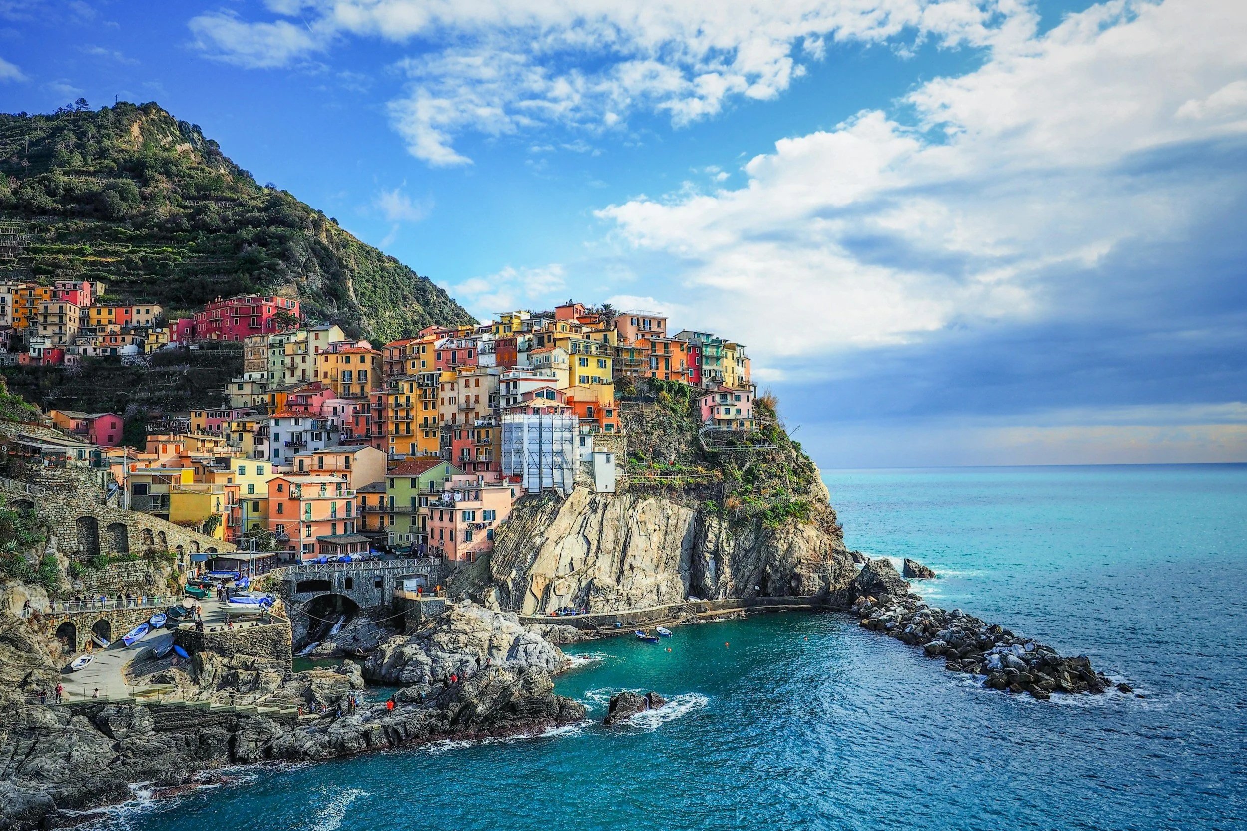 Colorful buildings perched on dramatic seaside cliffs overlooking the blue waters of Manarola in Cinque Terre, Italy.