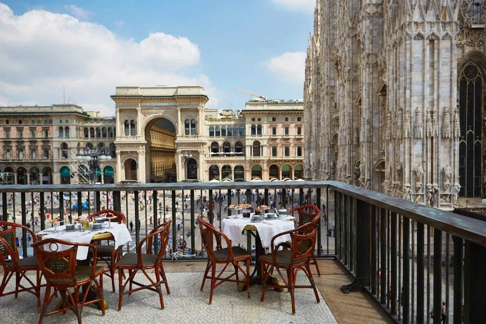 Outdoor dining terrace with breakfast tables overlooking Piazza del Duomo and Galleria Vittorio Emanuele in Milan, Italy.