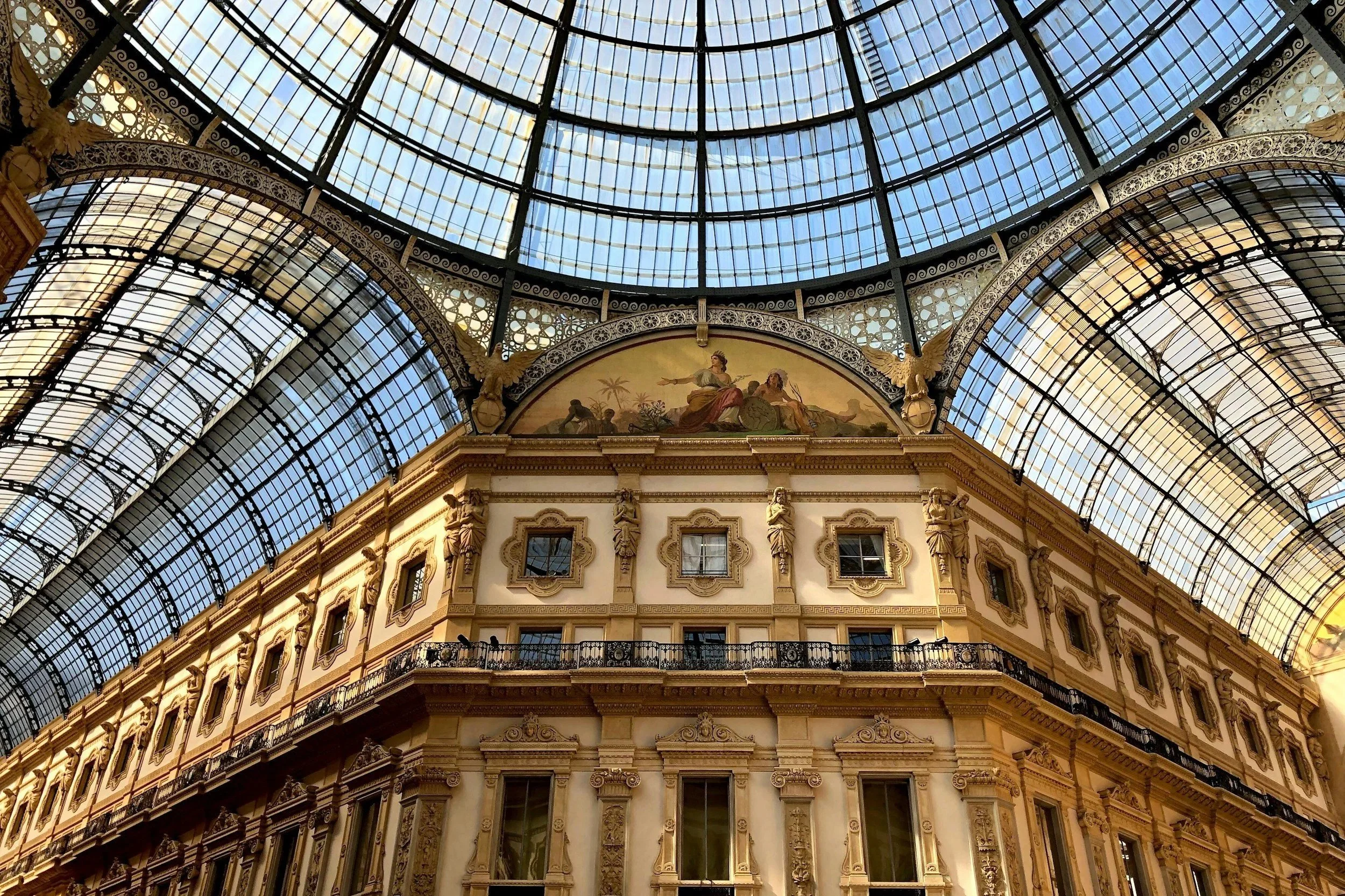 Low-angle view looking up at the intricate glass dome roof and classical facade inside the Galleria Vittorio Emanuele II in Milan