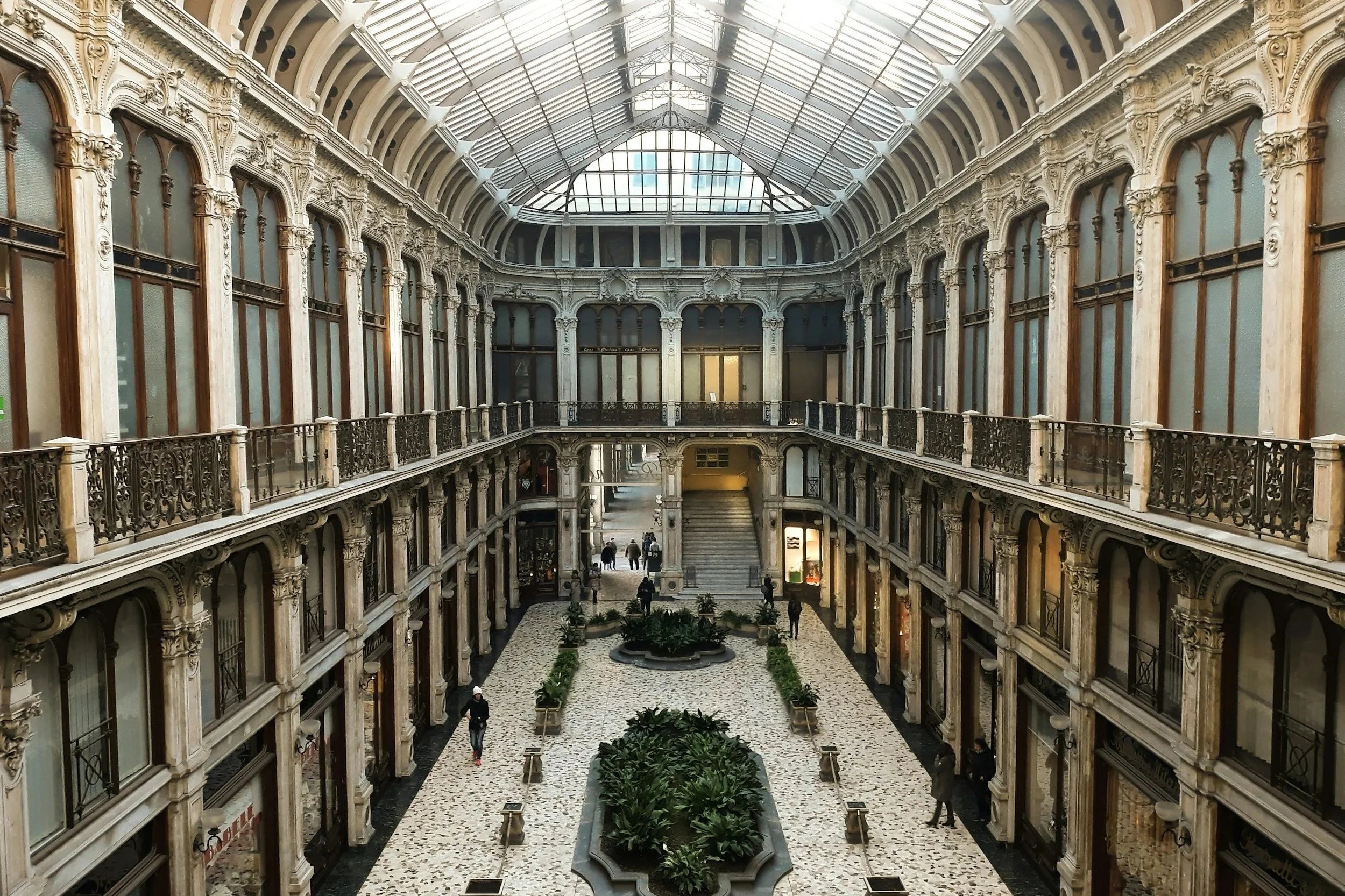 Interior view of Galleria Subalpina in Turin featuring wrought-iron balconies and an ornate glass barrel vault ceiling.