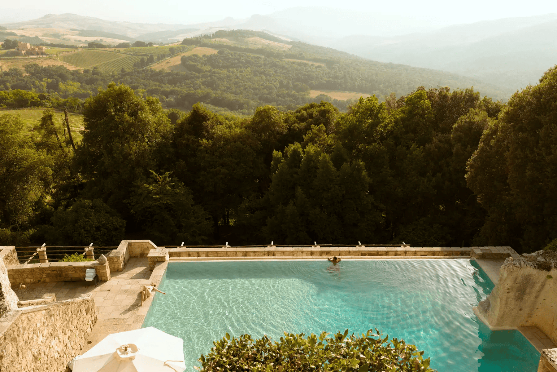Aerial view of a luxury infinity pool carved into stone cliffs overlooking rolling green hills at Borgo Pignano in Tuscany