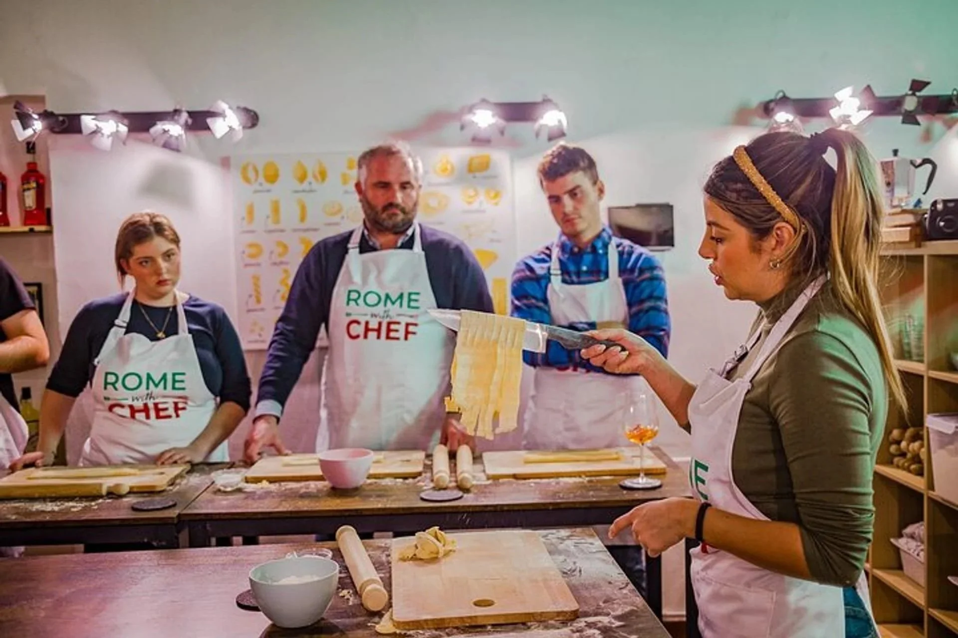 A chef demonstrating fresh handmade fettuccine pasta making with knife to students in a Rome cooking class.