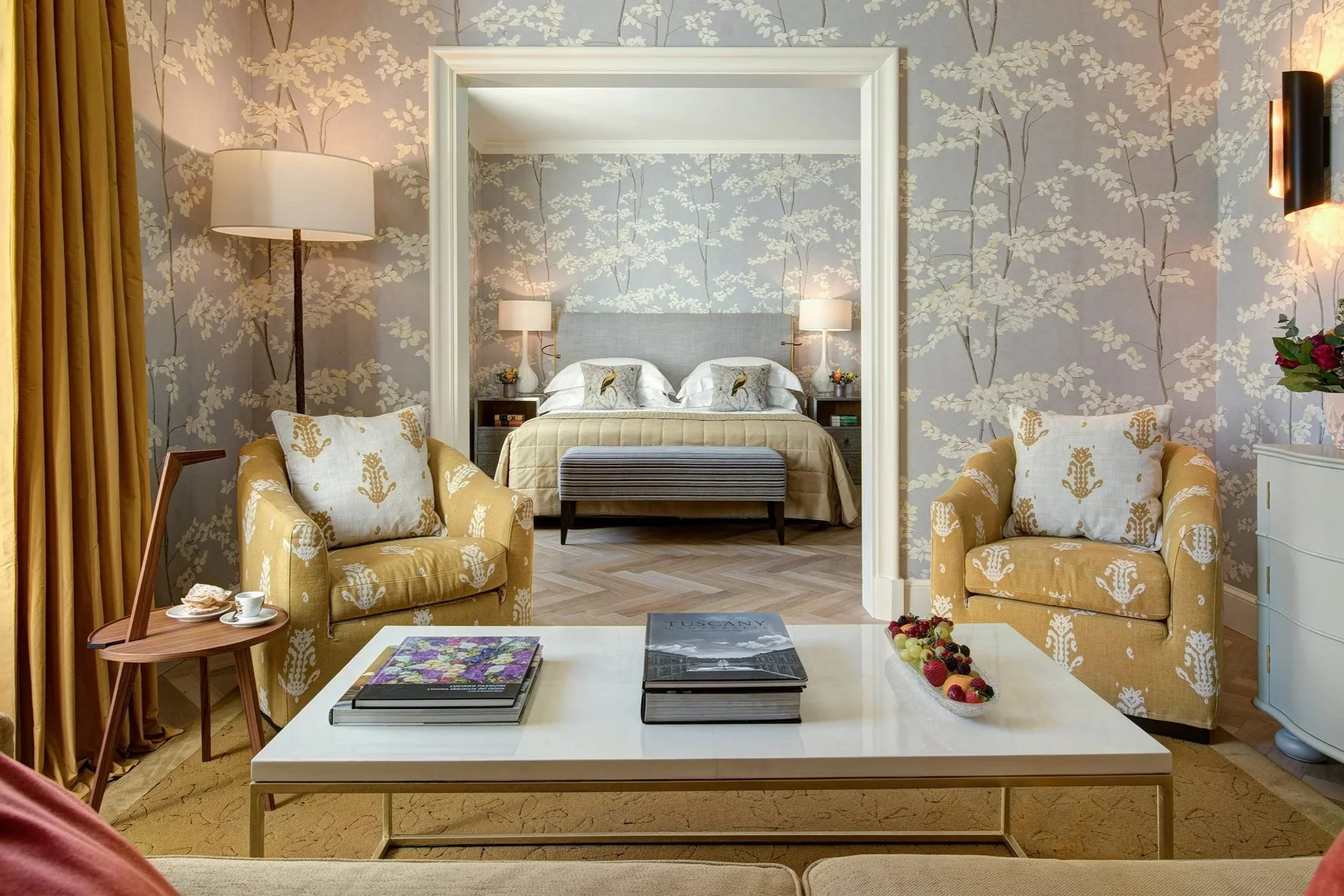 Luxury hotel suite in Florence with elegant seating area and king bed framed by floral wallpaper