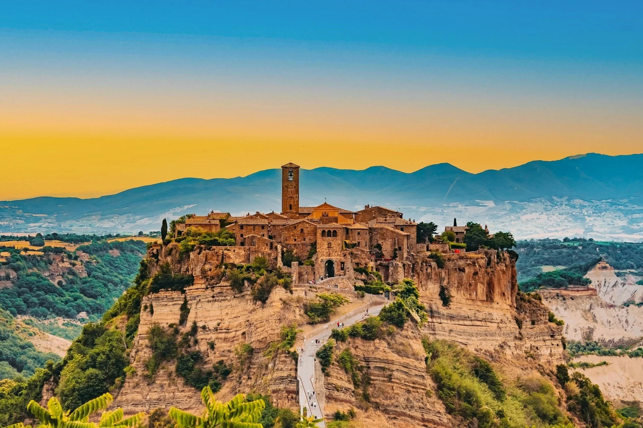 Pedestrian footbridge leading up to the ancient hilltop village of Civita di Bagnoregio perched on volcanic cliffside cliffs at sunset in Lazio, Italy.