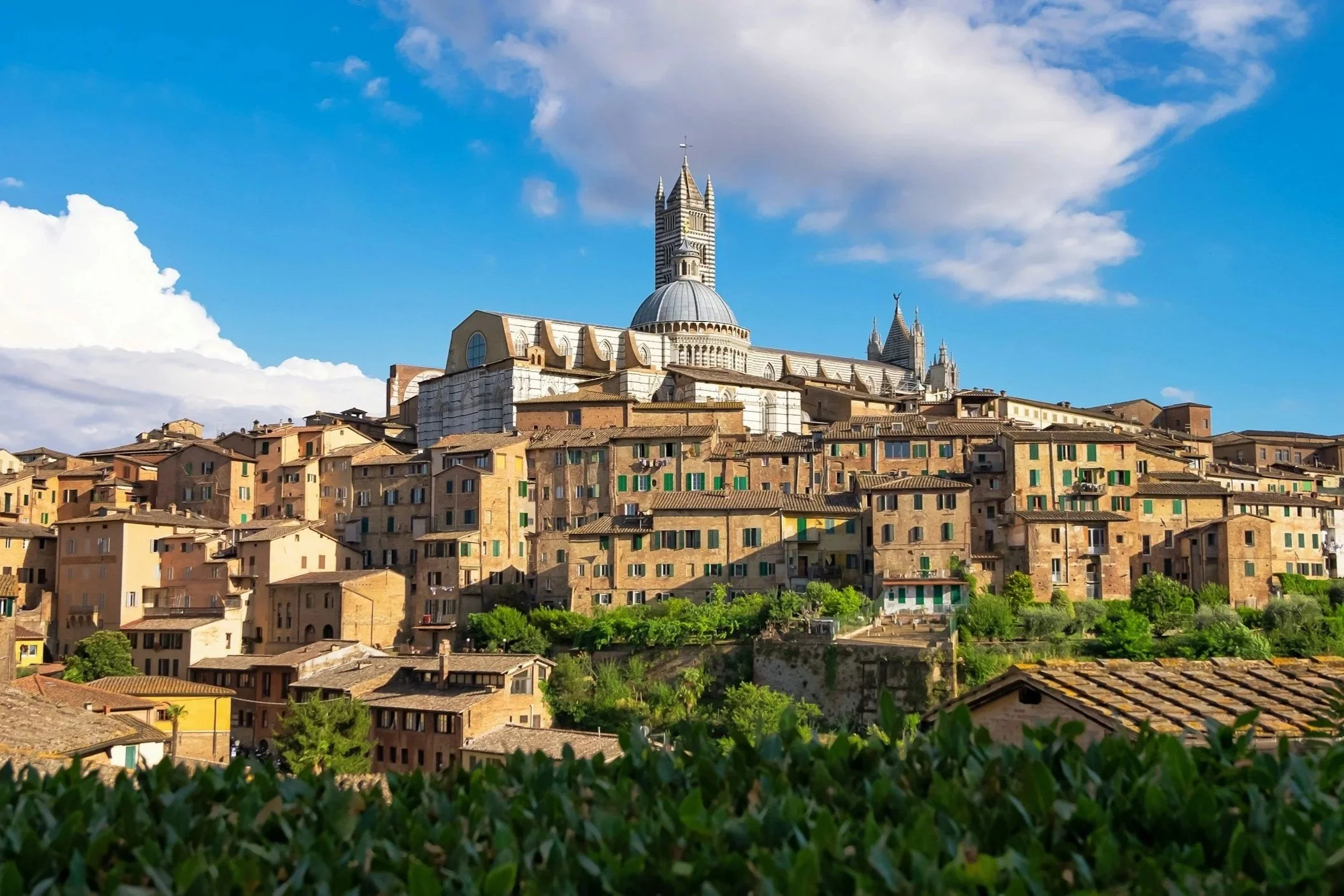 Panoramic view of the Siena Cathedral dome and bell tower rising above historic terracotta rooftops in Siena Italy