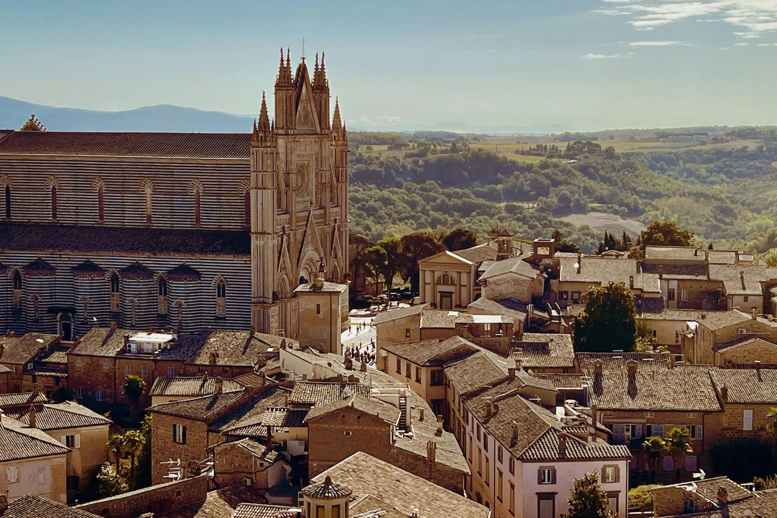 High-angle view of the Orvieto Duomo with its distinct striped marble facade towering over medieval terracotta rooftops and rolling Umbrian countryside