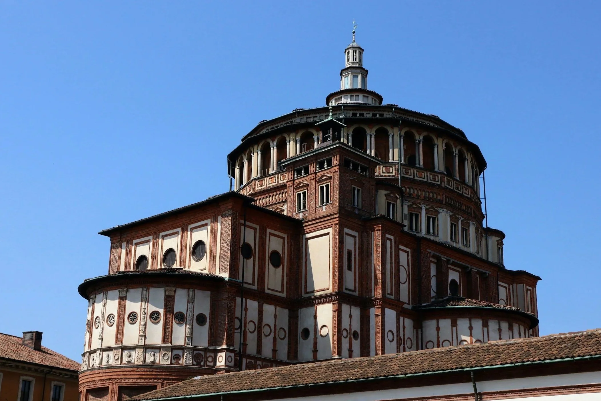 The Renaissance dome and exterior apse of Santa Maria delle Grazie church in Milan against a blue sky.