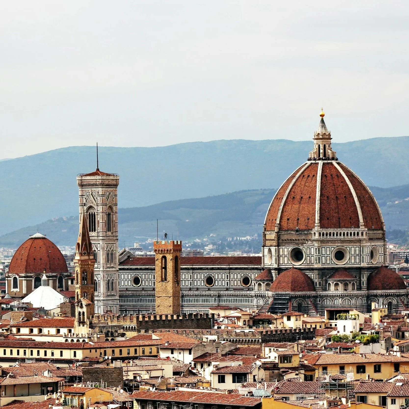 Panoramic skyline view of Florence featuring Brunelleschi's terracotta dome, Giotto's Campanile, and red clay rooftops framed by Tuscan hills.